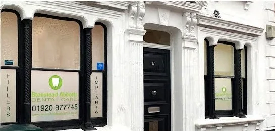 Exterior of a white building with a black front door, surrounded by two windows with black frames, one of which displays a dental care sign.