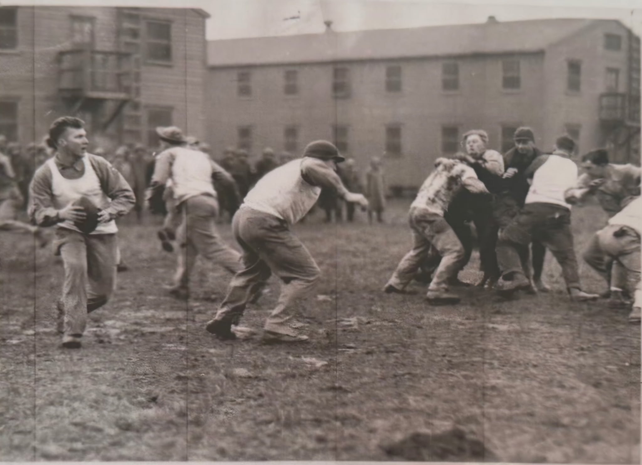Black and white photograph of children playing outdoors on a field, with some wearing baseball uniforms and others in casual clothing, and multi-story apartment buildings in the background.