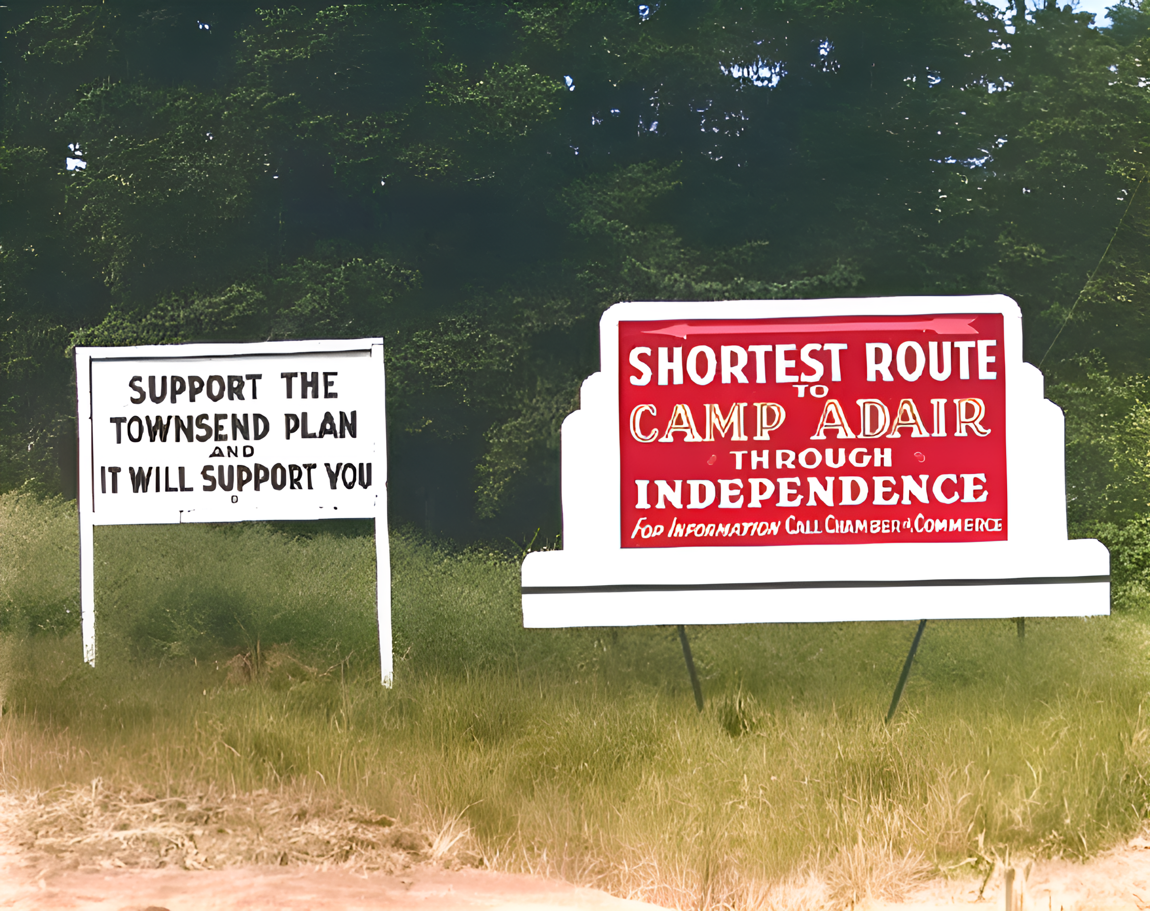 Two signs on a grassy area, one white with black text supporting townsend plan, the other red with white and yellow text indicating shortest route to Camp Adair through independence, with trees in the background.