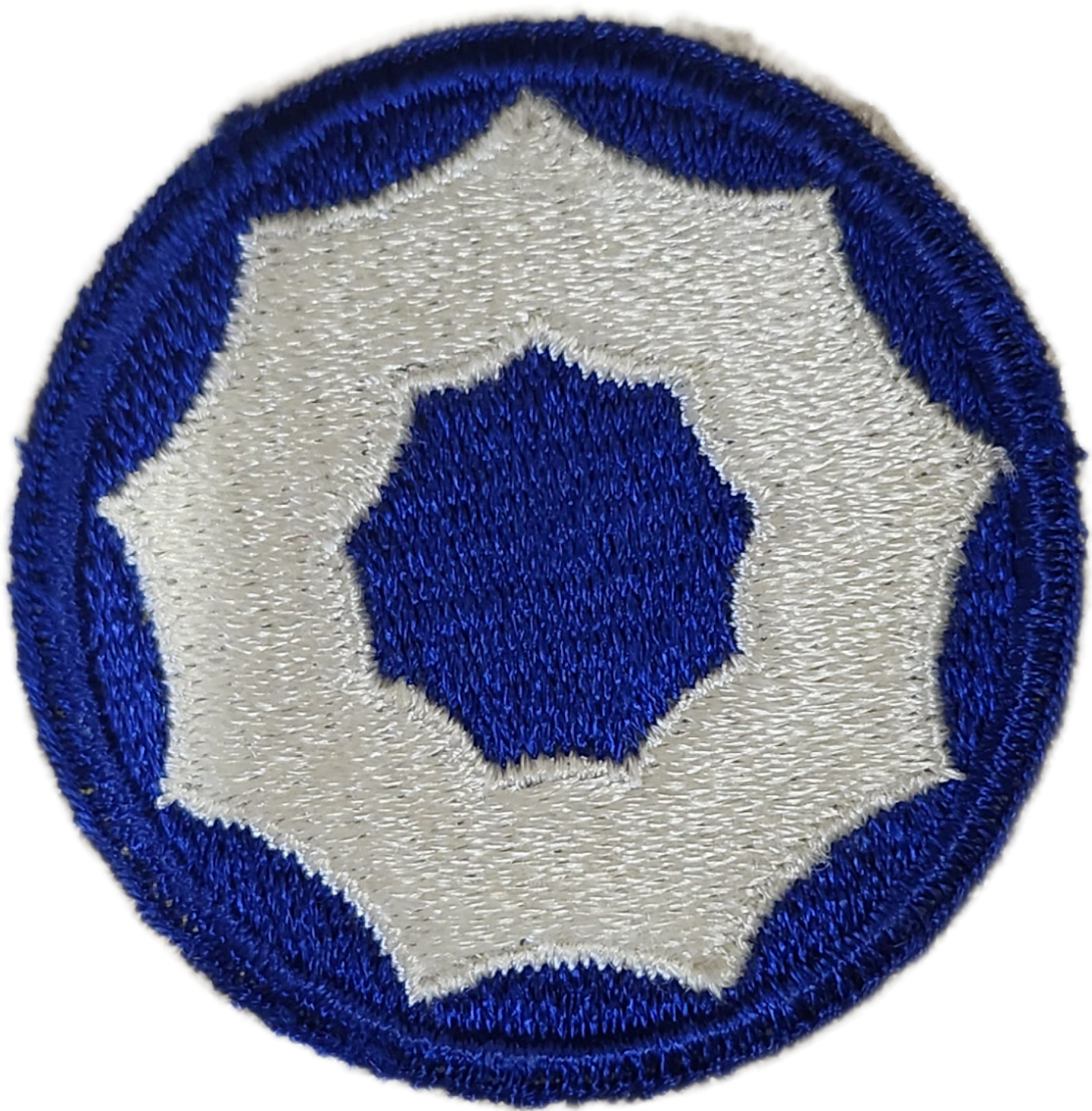 Close-up of a embroidered patch with a white background, a blue shield-shaped emblem in the center, and a blue ring border.