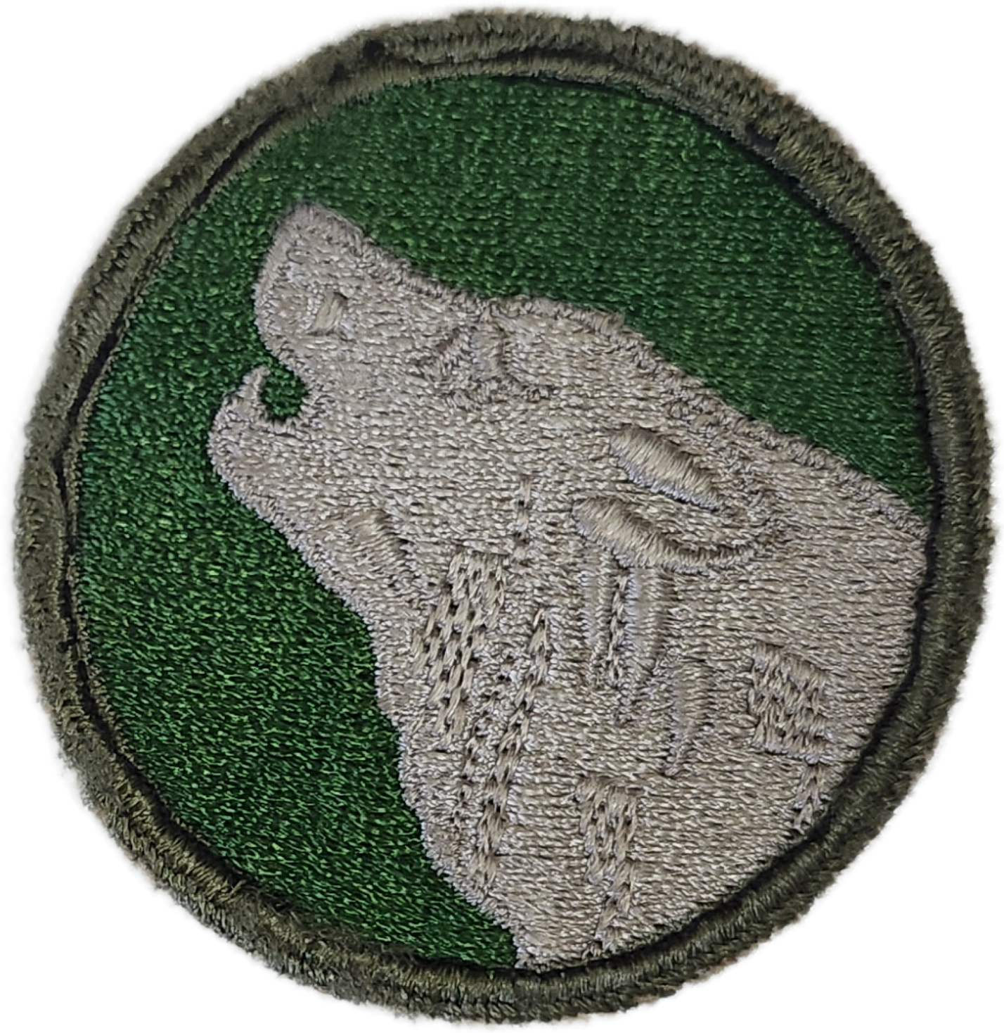 A military patch featuring a beige wolf with closed eyes and a helmet, set against a green background, with a black border.