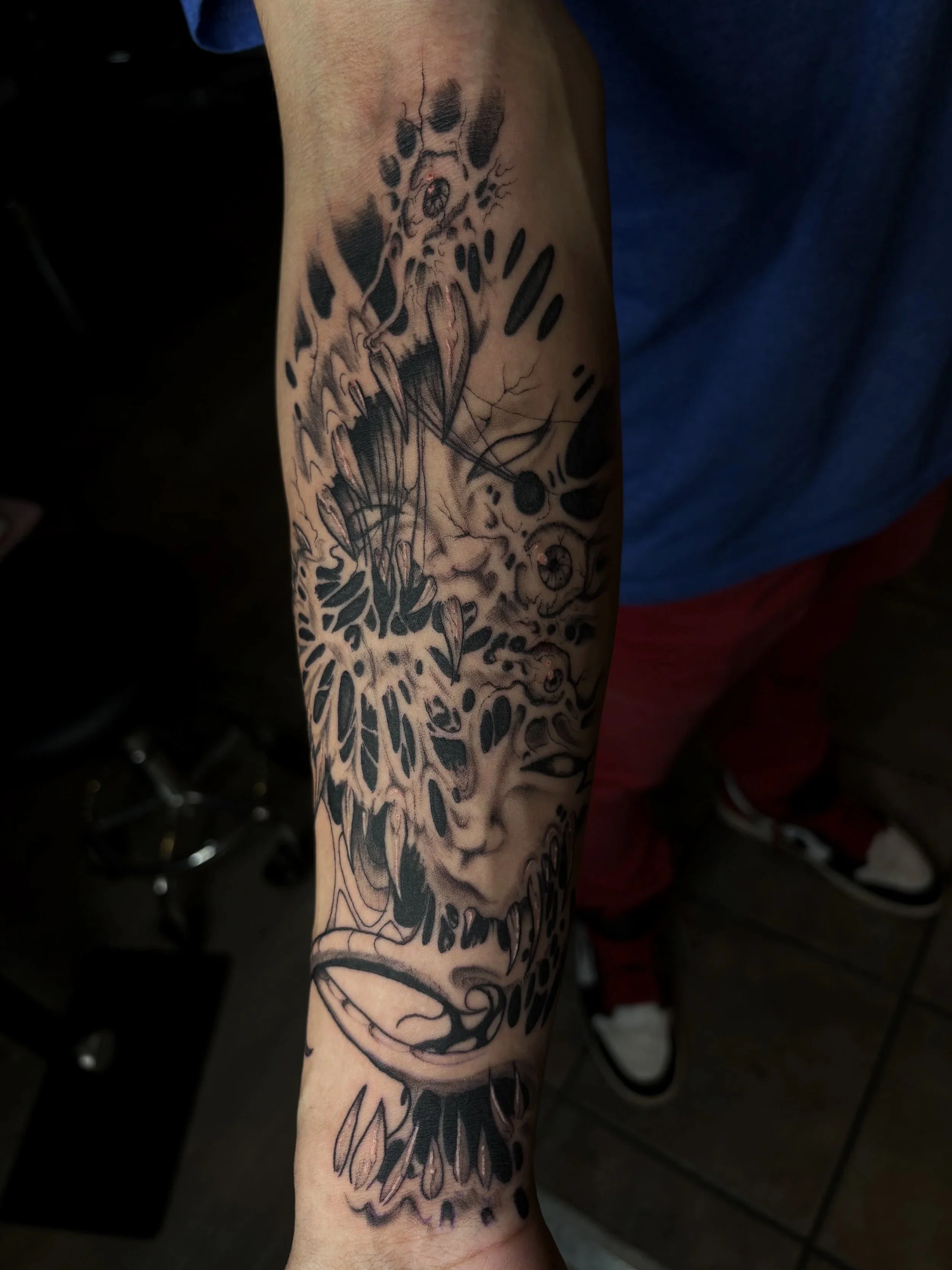 A tattoo on a person's arm featuring a skull with floral and abstract elements, predominantly black ink with intricate line work and shading.