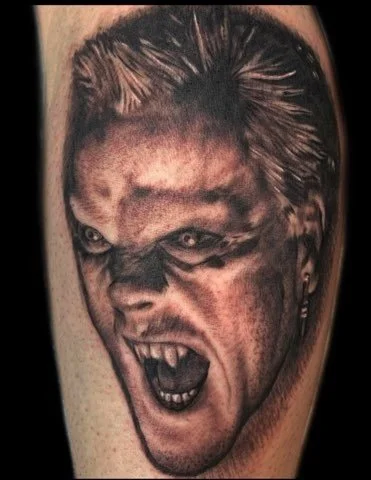 Tattoo of a woman's face with an angry, fierce expression, showing teeth and snarling.