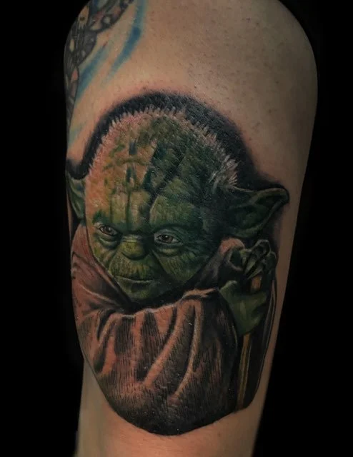 Tattoo of Yoda from Star Wars holding a cane, with a forest scene and trees reflected in his head.