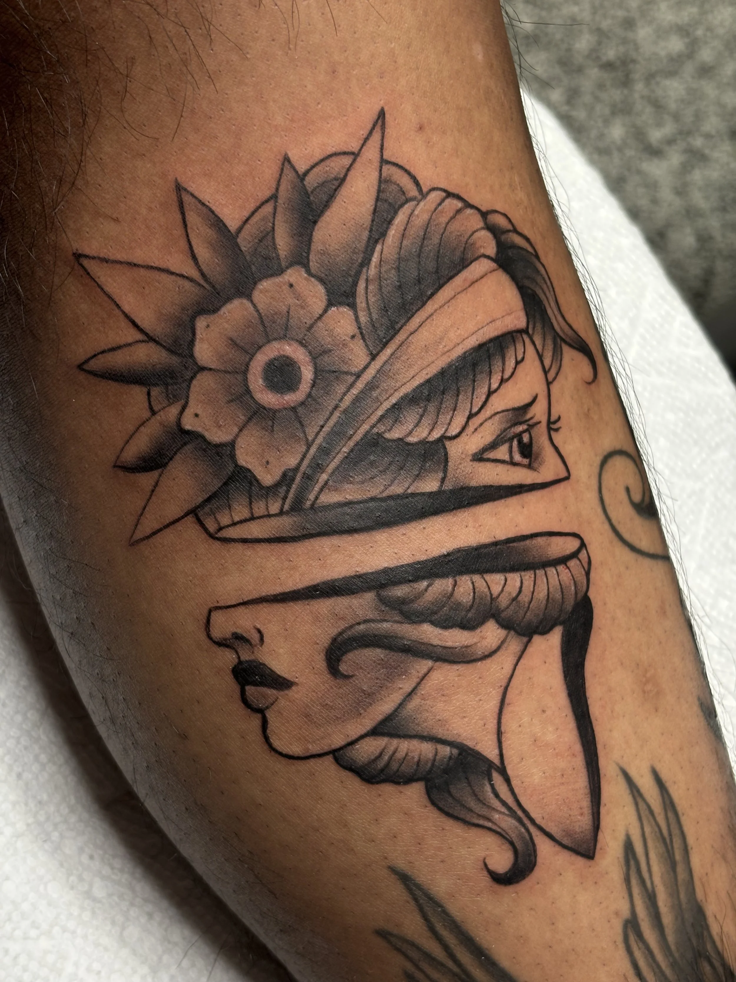 A tattoo of a woman's face with a flower headpiece and leaves on the person's upper arm.