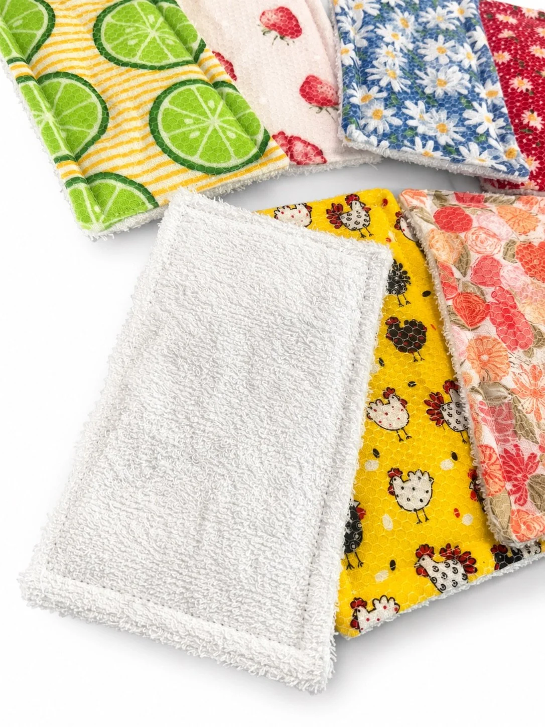 Stack of colorful patterned washcloths and white textured towels, including citrus, strawberry, daisy, floral, and cartoon animal designs