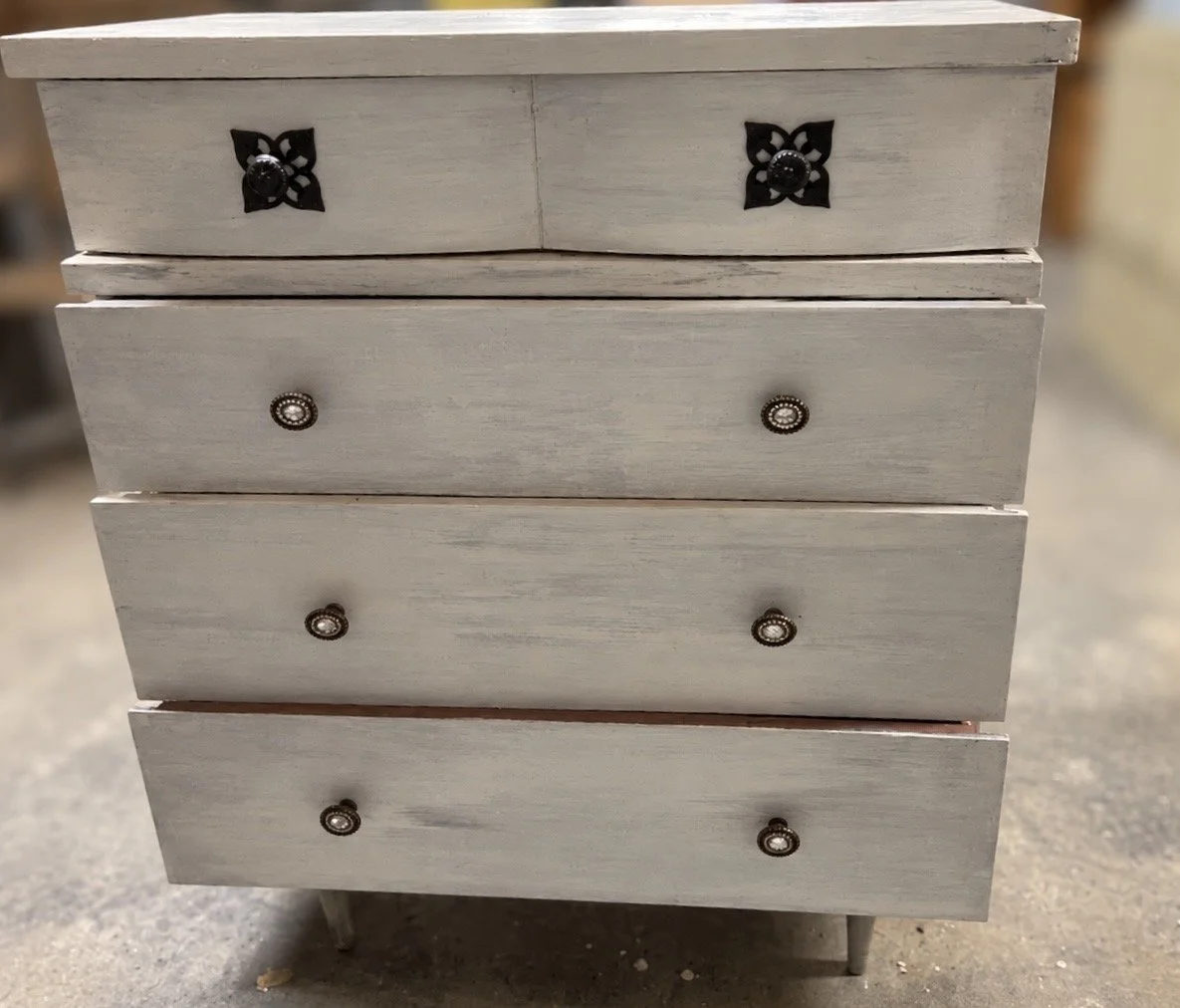 Distressed white wooden chest of drawers with four drawers and decorative black and brass handles