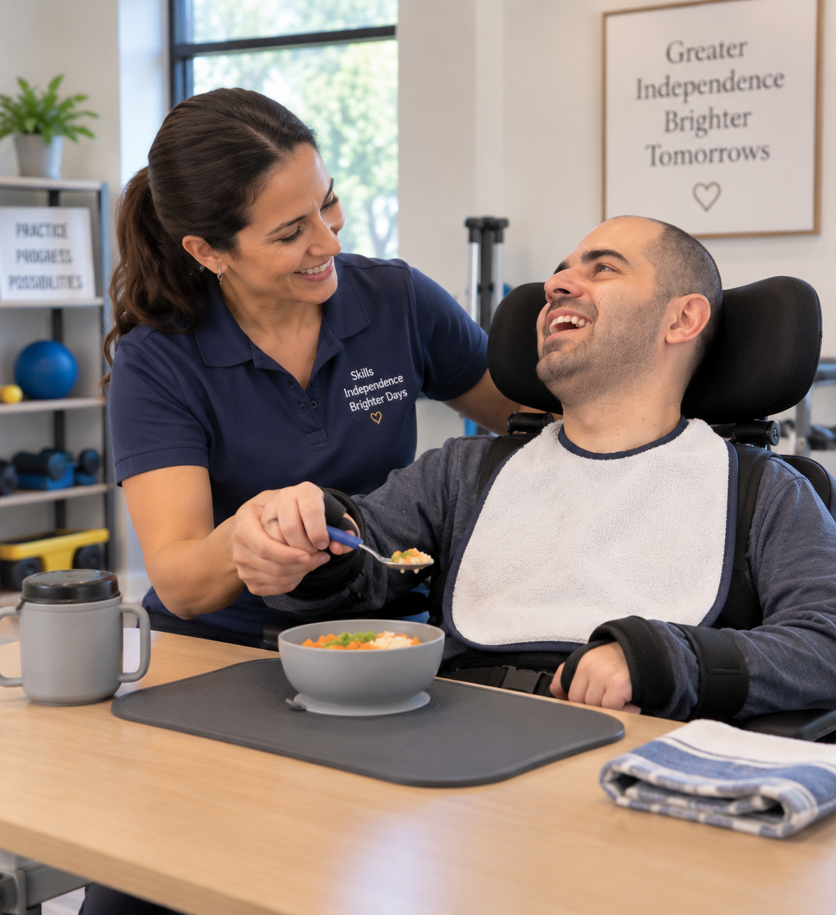 A caregiver feeds a man in a wheelchair, smiling and sharing a moment together in a therapy or care setting, with motivational signs and equipment in the background.
