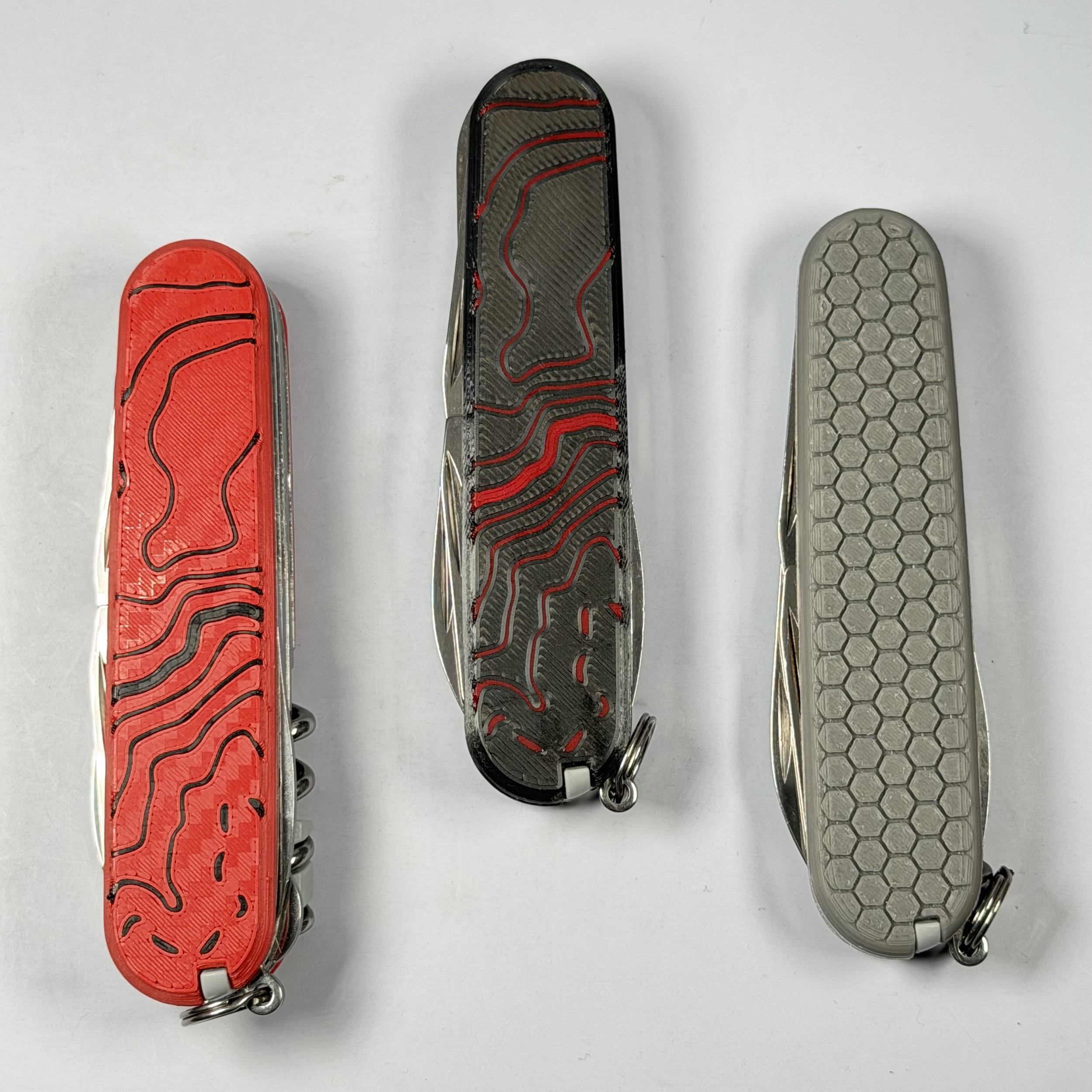 Three multi-tool pocket knives with different textured handles and integrated keyrings on a white surface.