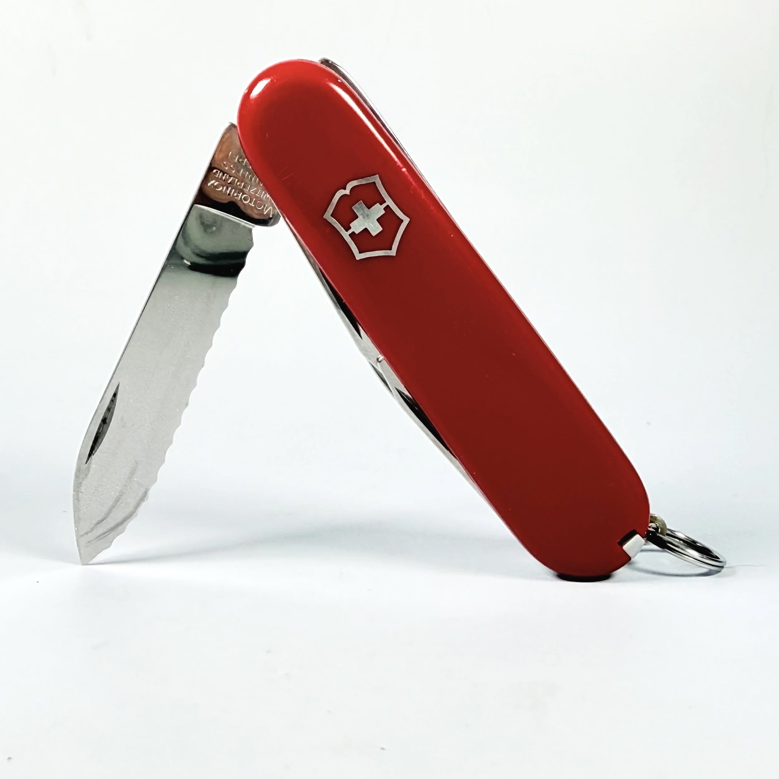 Close-up of a Swiss Army knife with a red handle and a partially extended blade, placed against a plain white background.