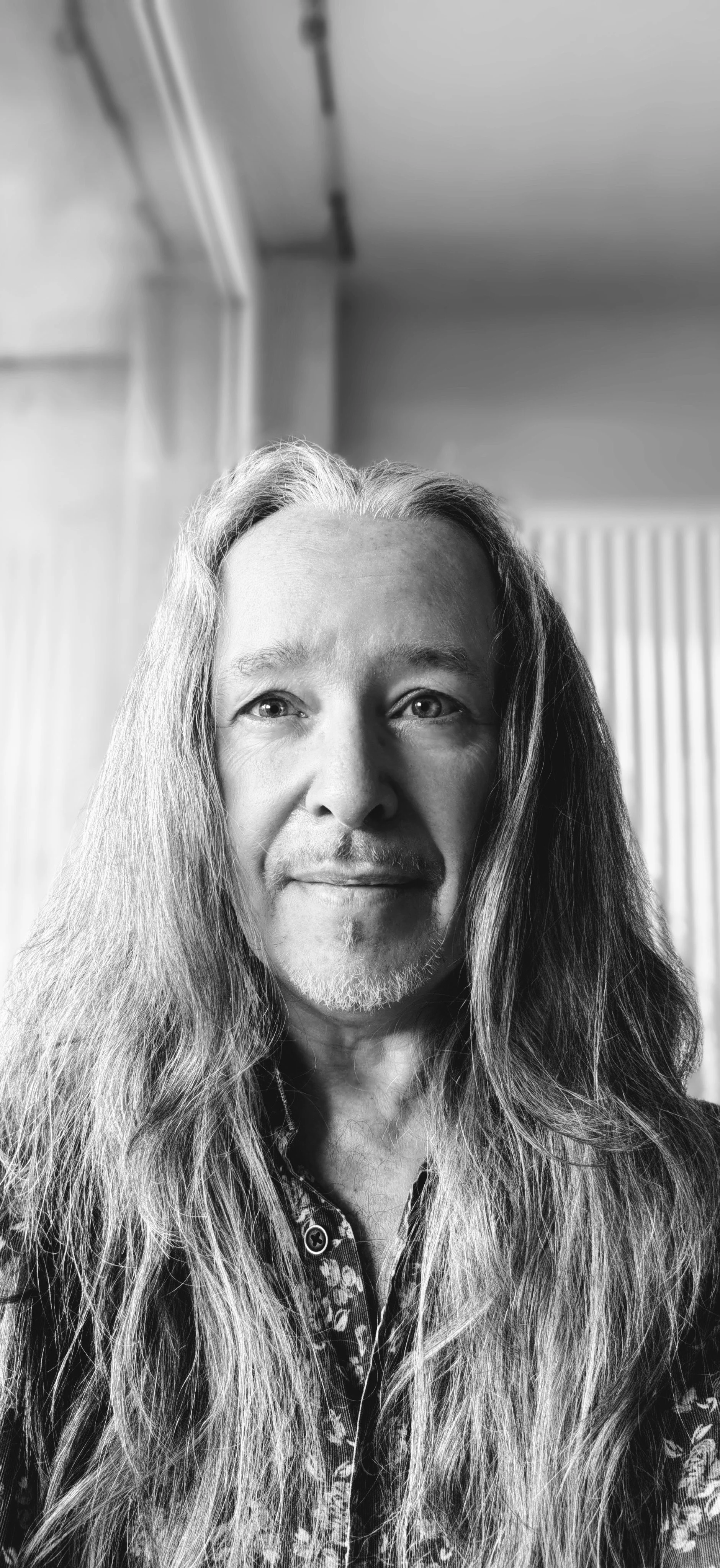 Beautiful black and white portrait of a middle-aged man with long hair and a slight beard and soul patch, smiling, light indoors surroundings, mysti spiritual artistic vibe.