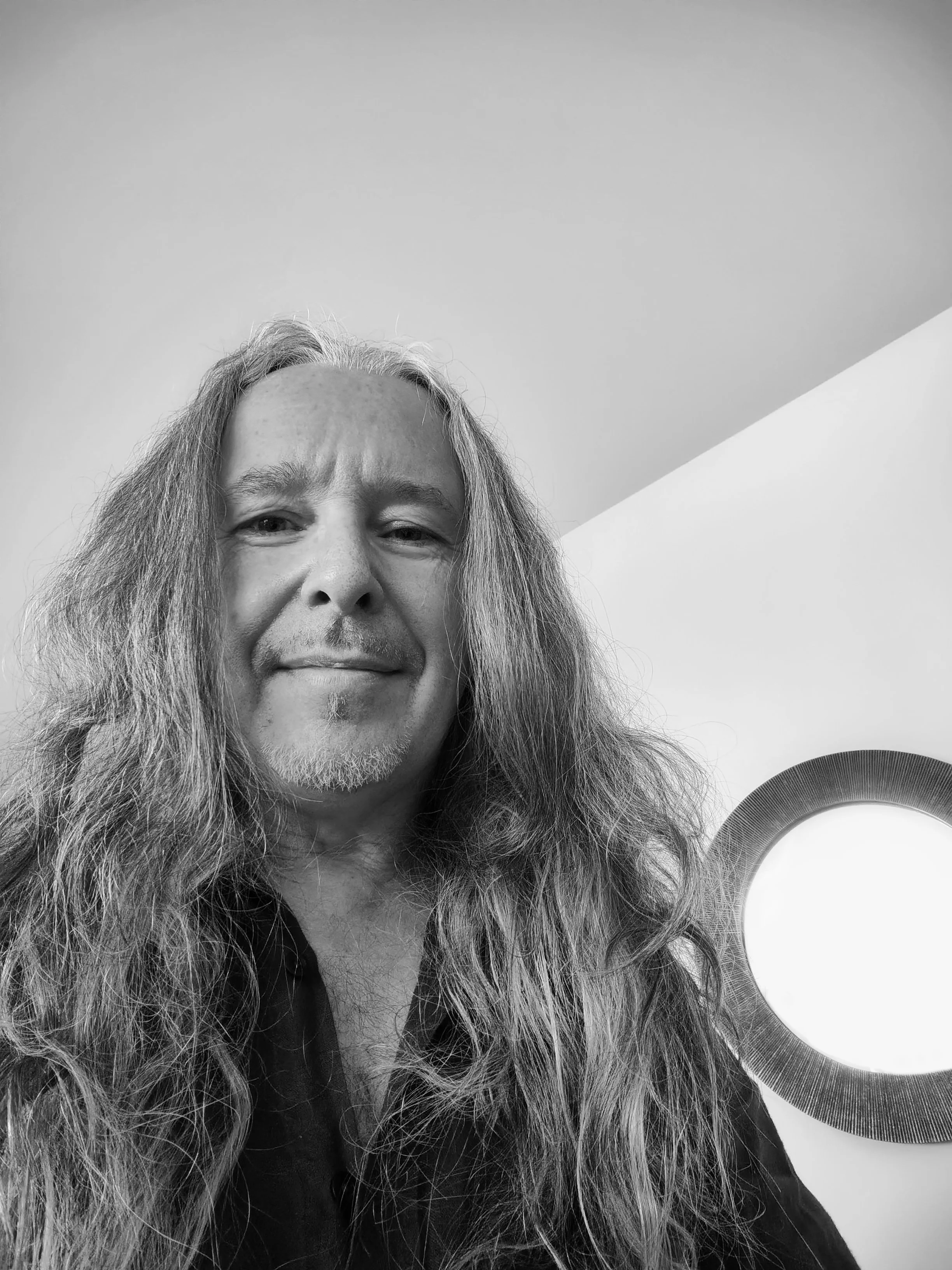 Beautiful black and white portrait of a middle-aged man with long hair and a slight beard and soul patch, smiling, light indoors surroundings, mysti spiritual artistic vibe.