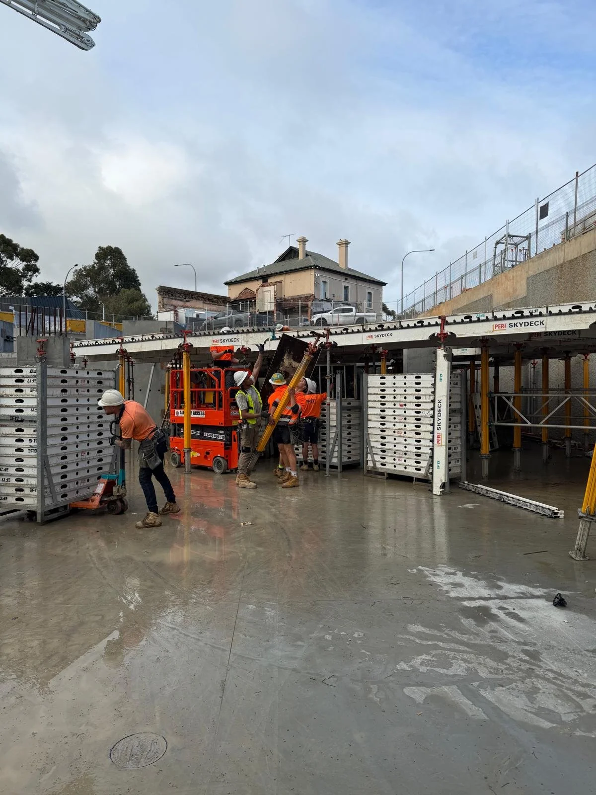 Construction workers installing structural elements at a construction site during daytime, with residential buildings in the background.