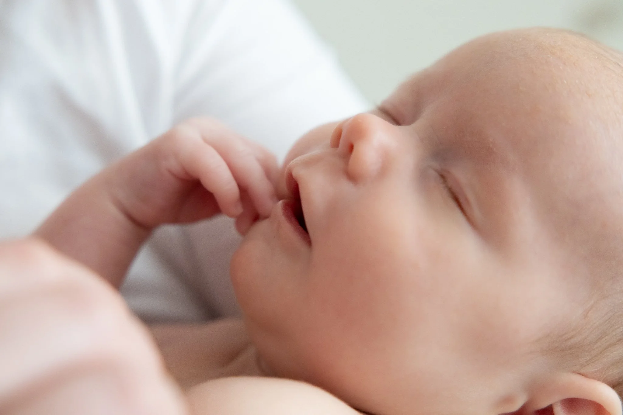 A close-up of a baby with eyes closed, holding a finger.