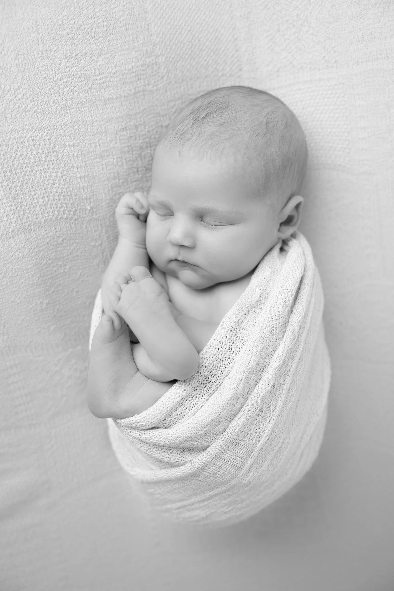 A sleeping baby wrapped in a soft blanket, resting against a textured wall.