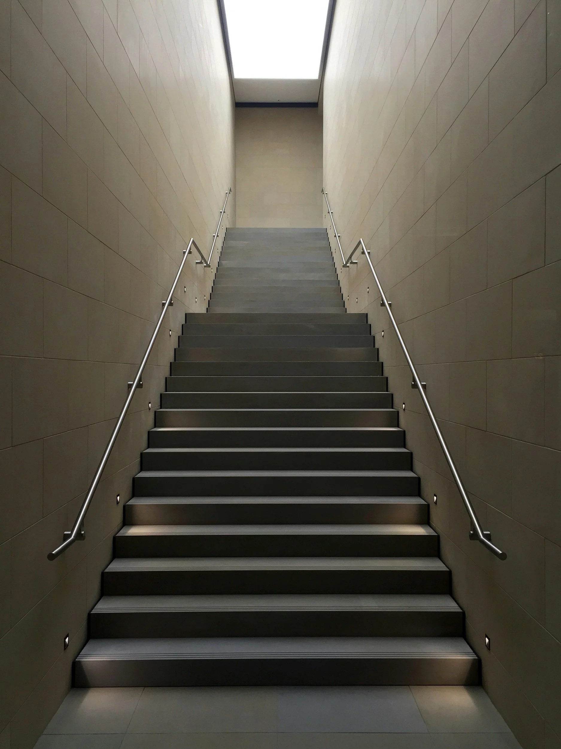 Staircase with handrails leading toward daylight.