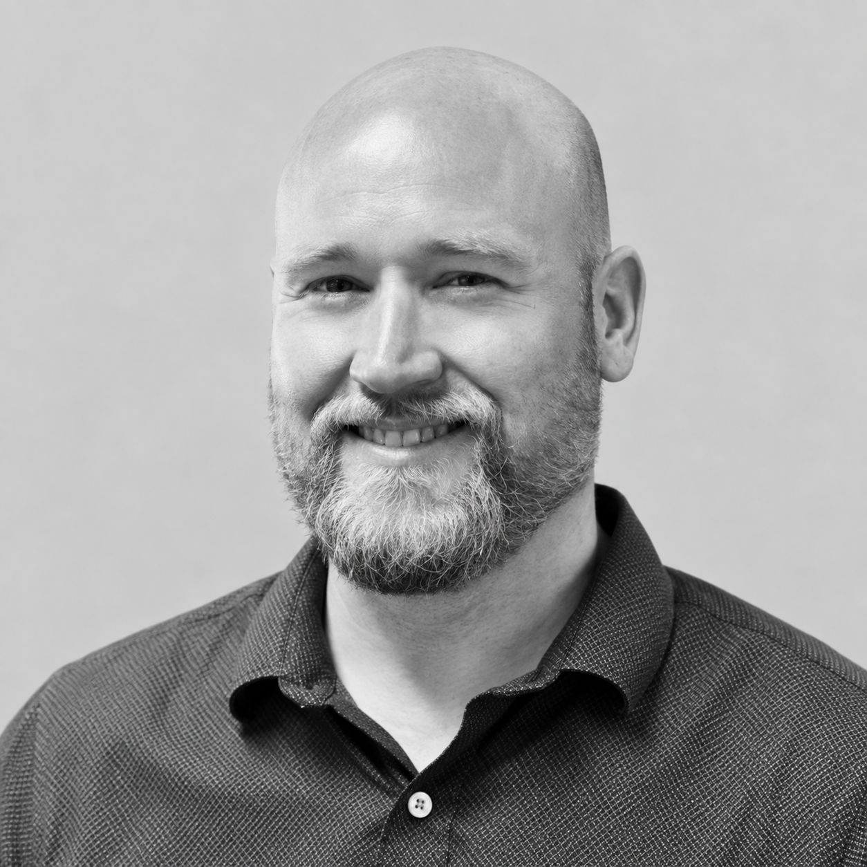 Greg LaSalle - A black and white portrait photograph of a smiling man with a bald head, beard, and mustache, wearing a collared shirt.