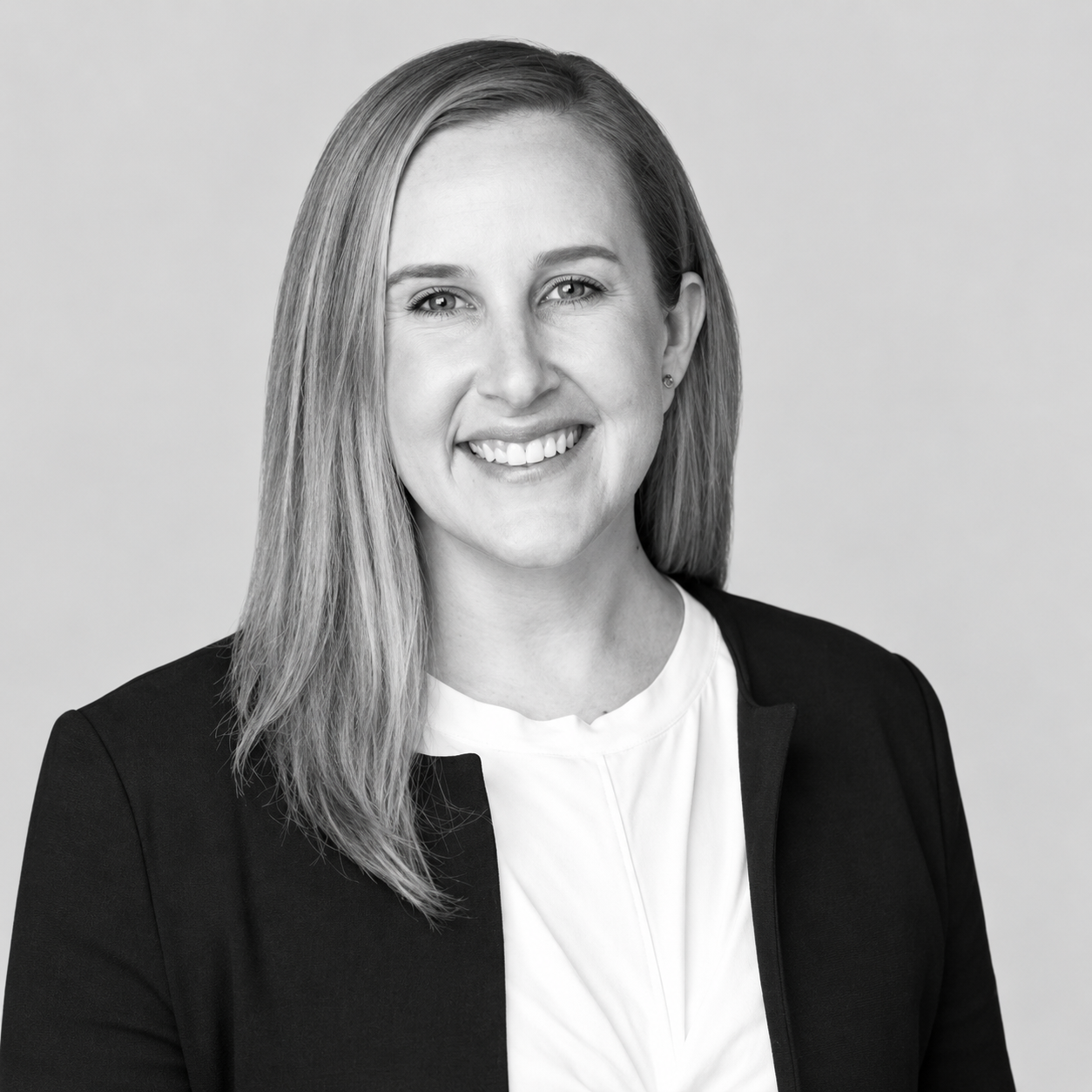 Mollie Scozzari - Black and white headshot of a smiling woman with straight, shoulder-length hair, dressed in business attire, against a plain background.
