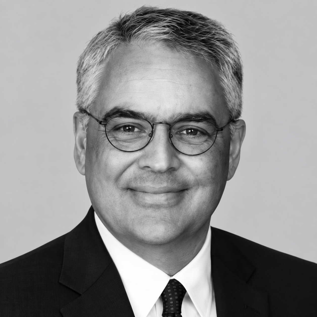 Mike Berthelsen - Black and white portrait of a middle-aged man with gray hair, glasses, wearing a suit and tie, smiling.