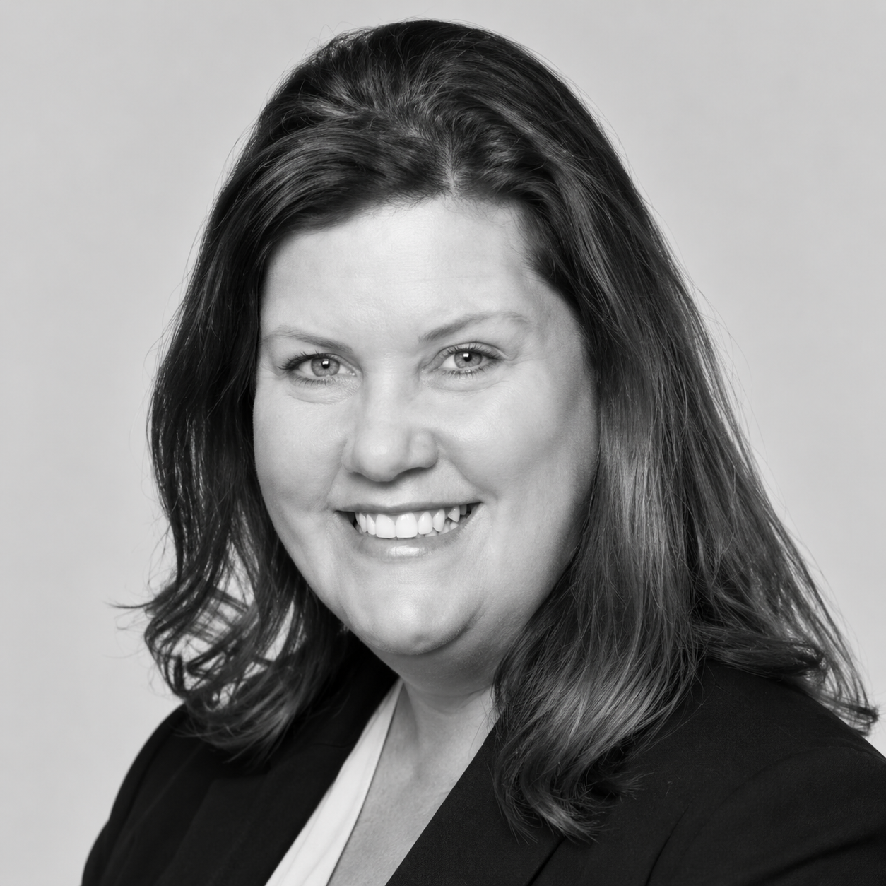 Donna Pinotti - Black and white portrait of a woman smiling, with shoulder-length wavy hair and wearing a blazer.