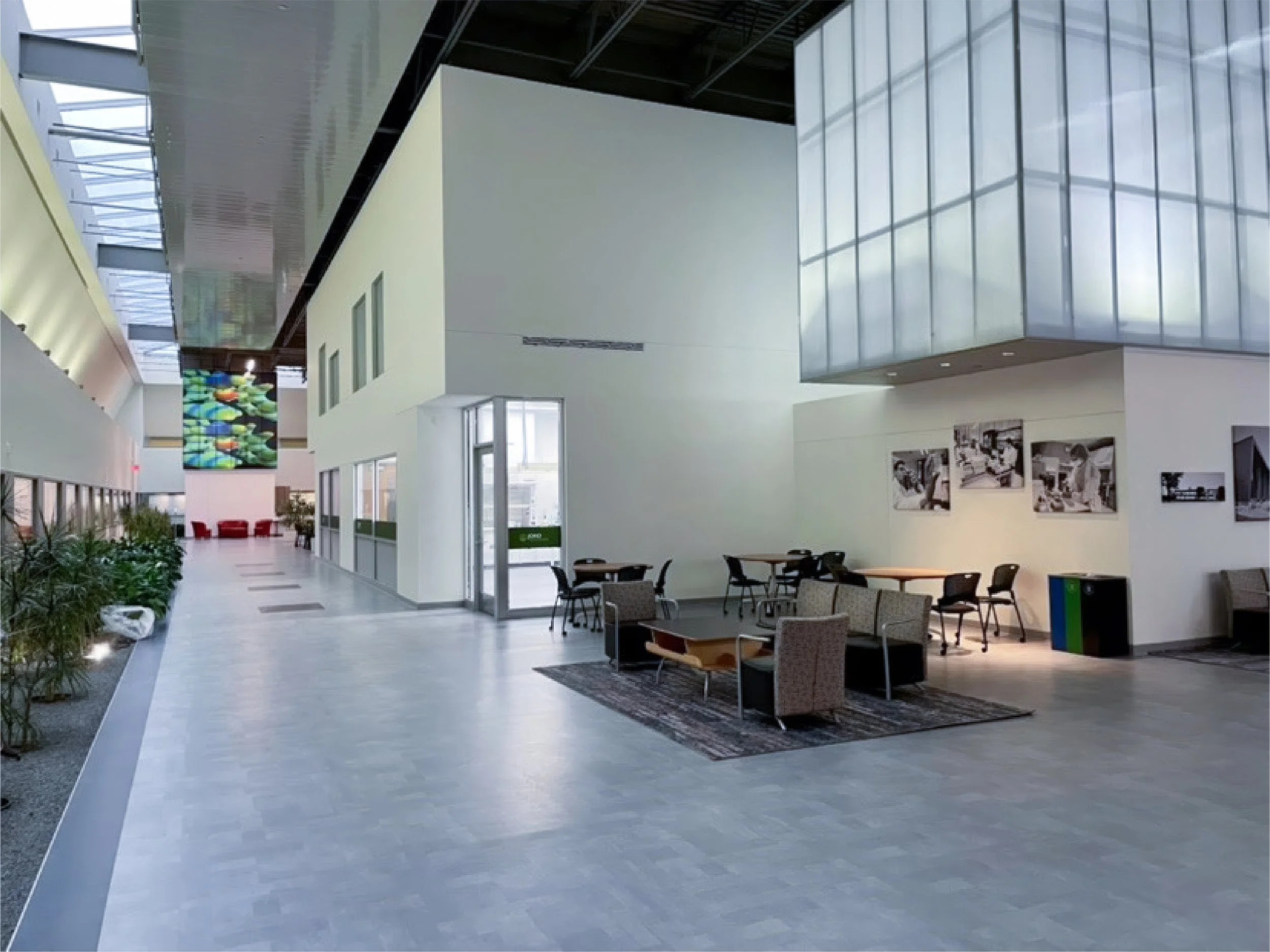 Interior of a modern building lobby with seating areas, large windows, and an art piece on the wall.