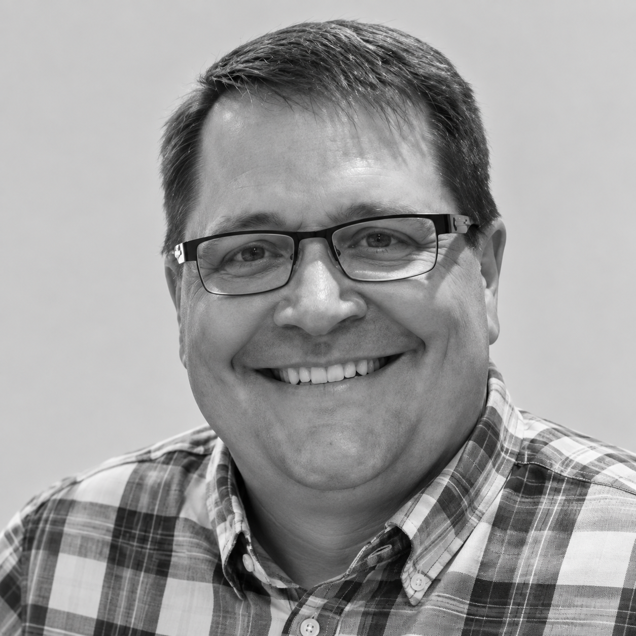 Jay Beyer-Kropuenske - A smiling man with glasses in a plaid shirt, black and white photo.