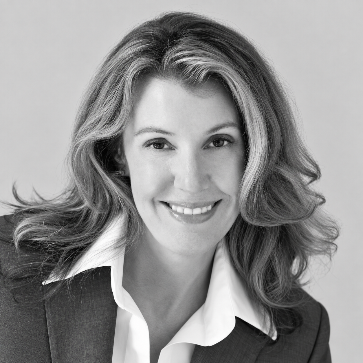 Barbara Nelsen - Black and white headshot of a smiling woman with wavy hair, wearing a blazer and white shirt, against a plain background.
