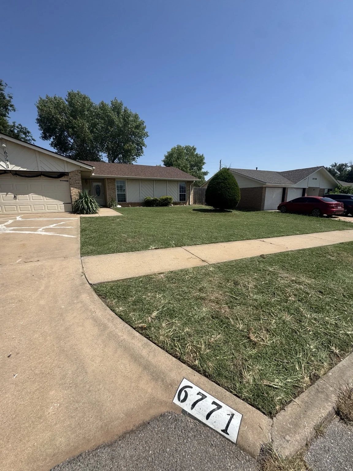 Front view of two single-story residential houses with driveways, cars parked outside, and a well-maintained lawn in a suburban neighborhood.
