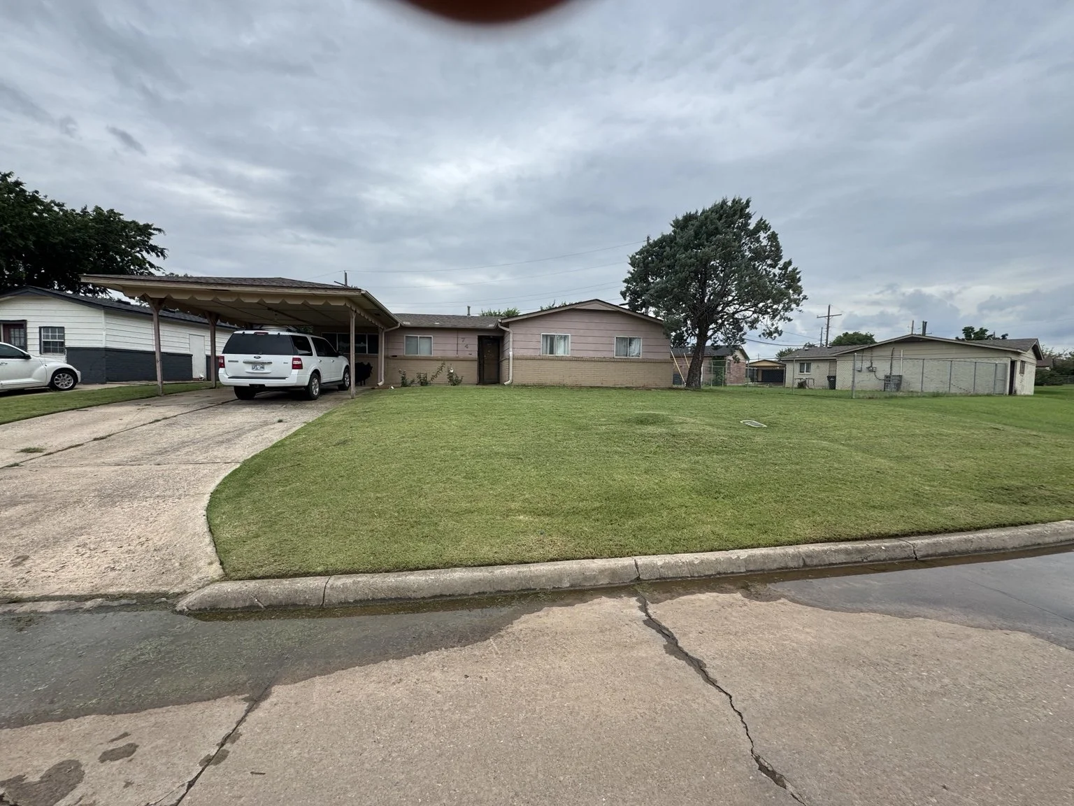 A residential house with a driveway and carport, green lawn, and cloudy sky.