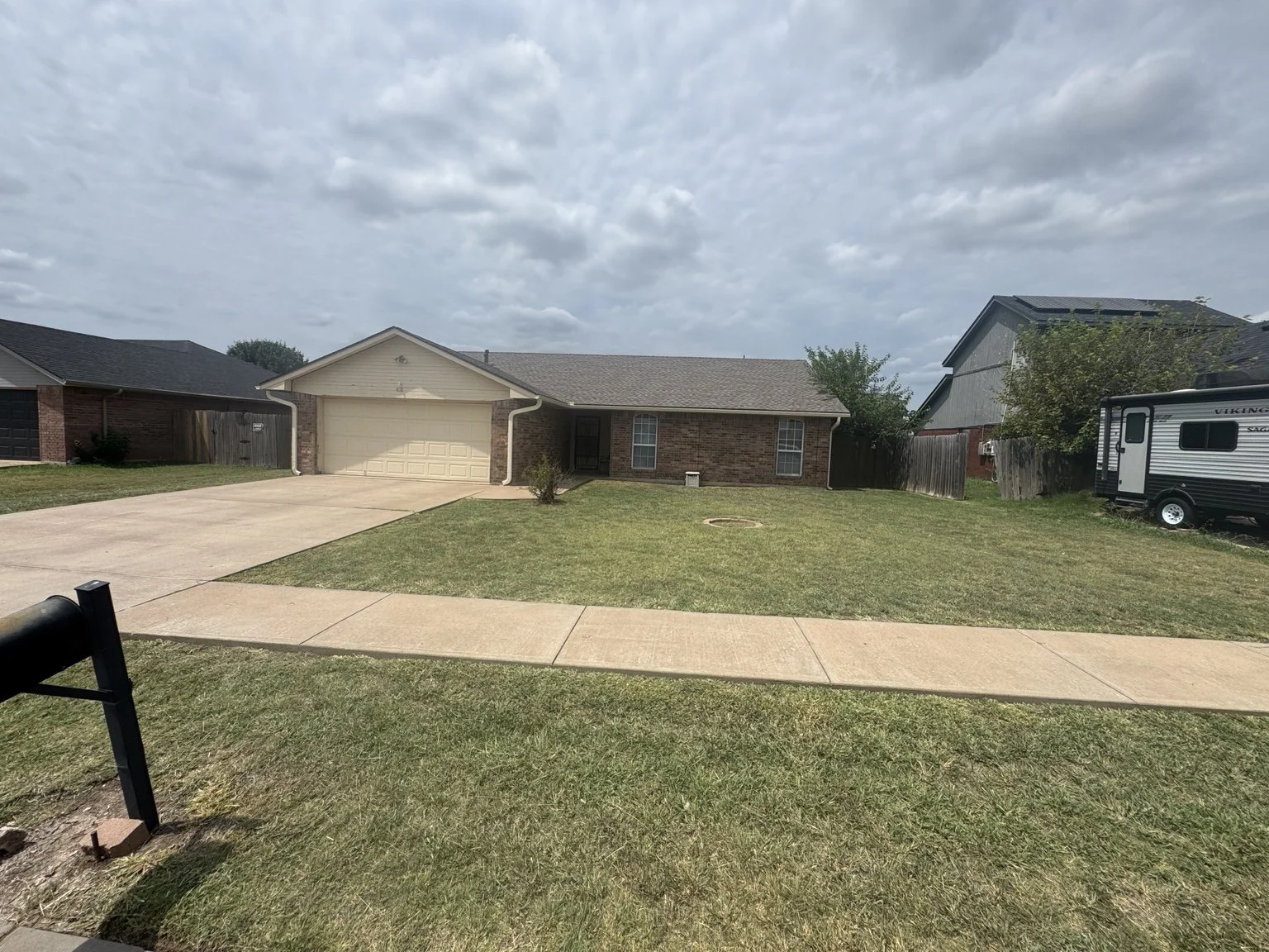 Front yard and house of a suburban home with driveway, small tree, and a traveling trailer parked to the side.