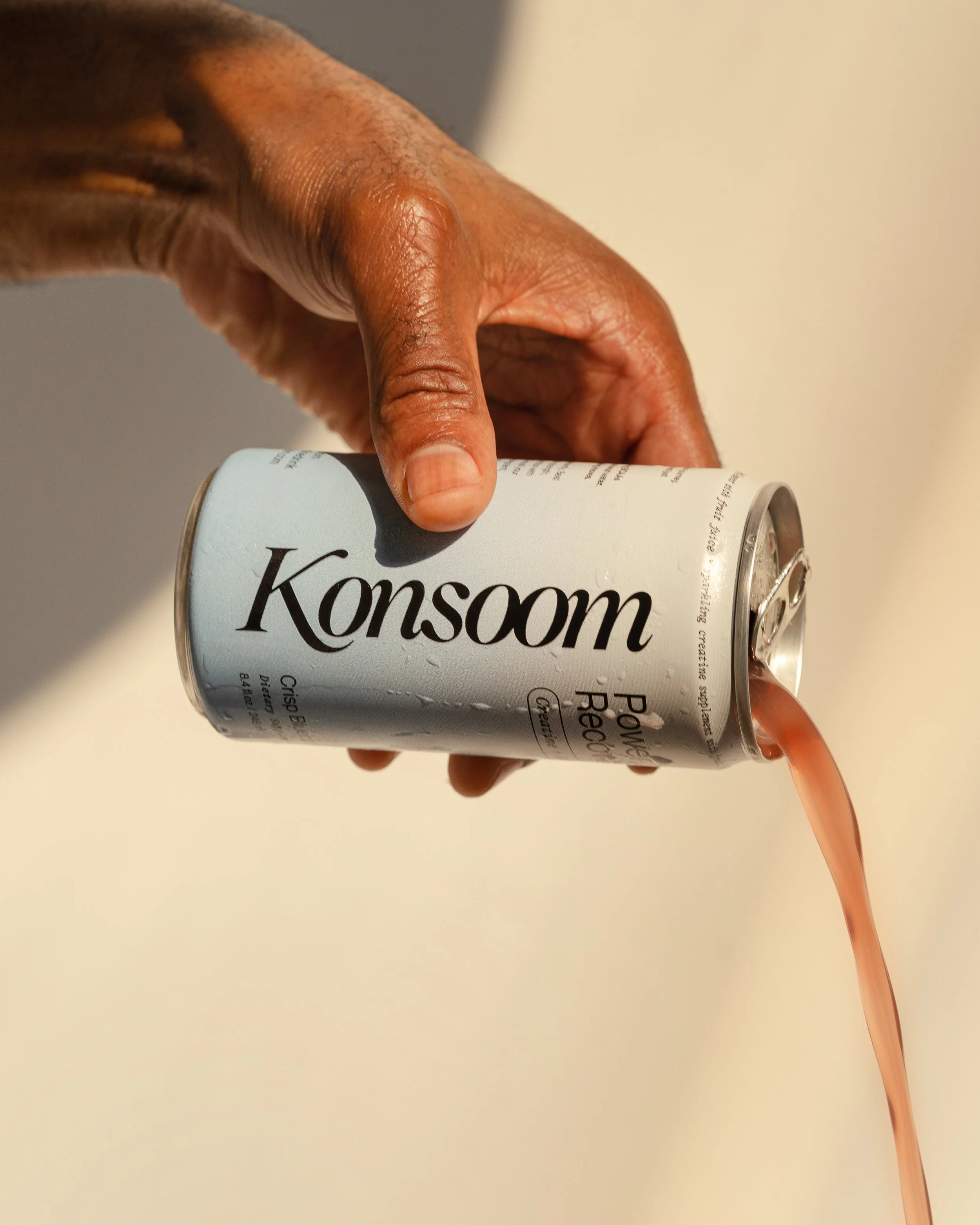 Hand pouring a Konsoom Power & Recovery beverage from a can into a glass.