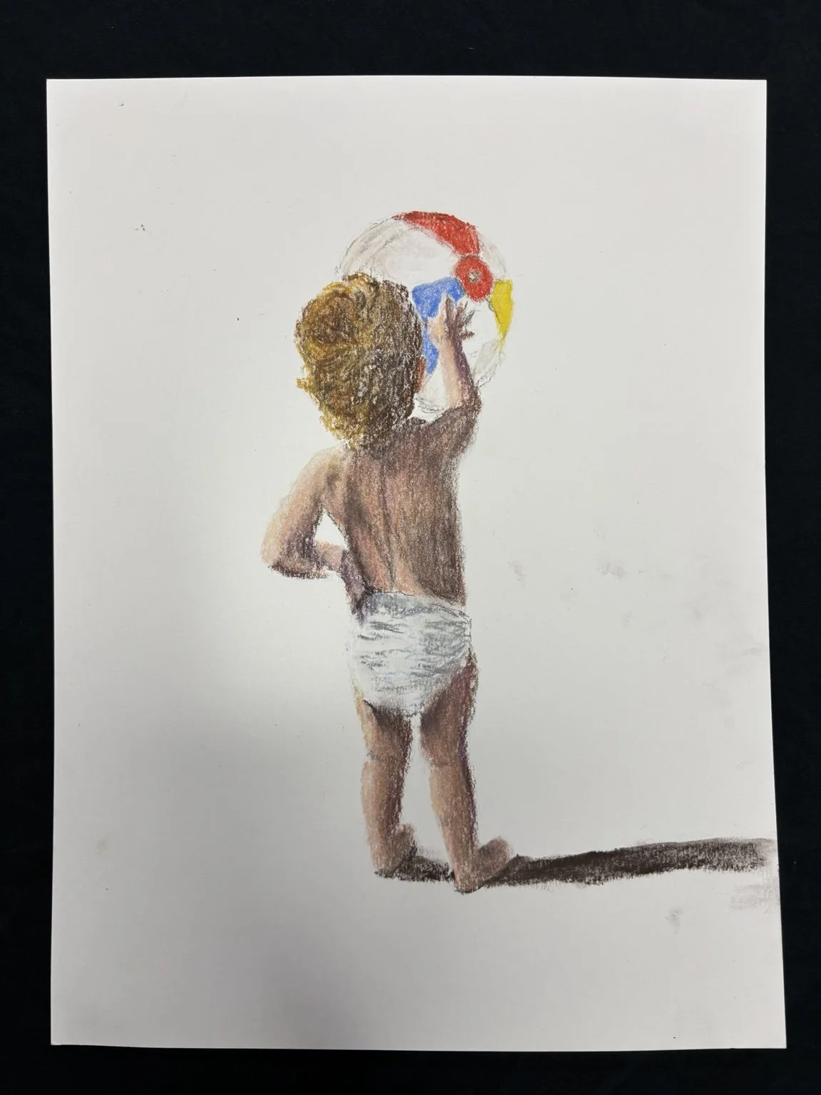Child with curly hair in a diaper painting a large, colorful face on a wall or paper.