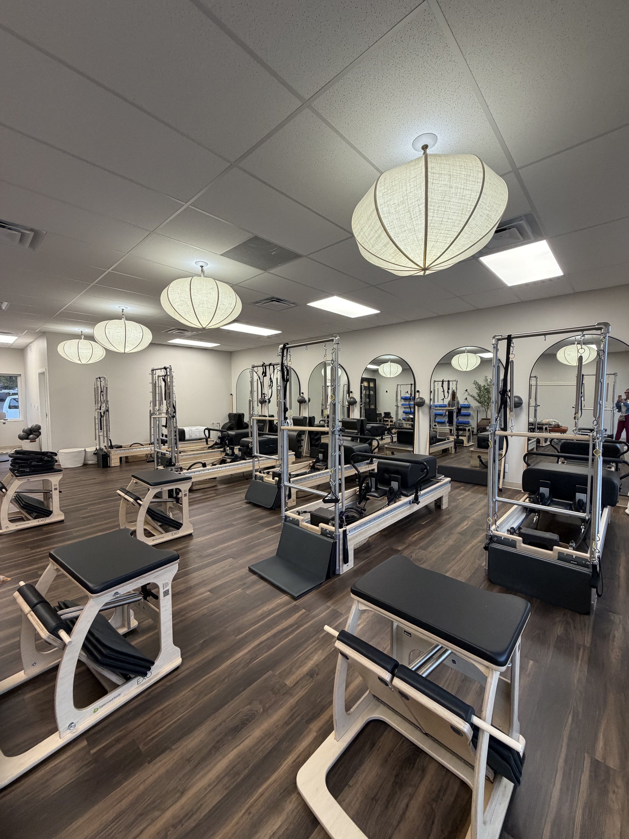 A fitness studio with reformer Pilates machines, mirrors on the wall, and modern lighting fixtures on the ceiling.