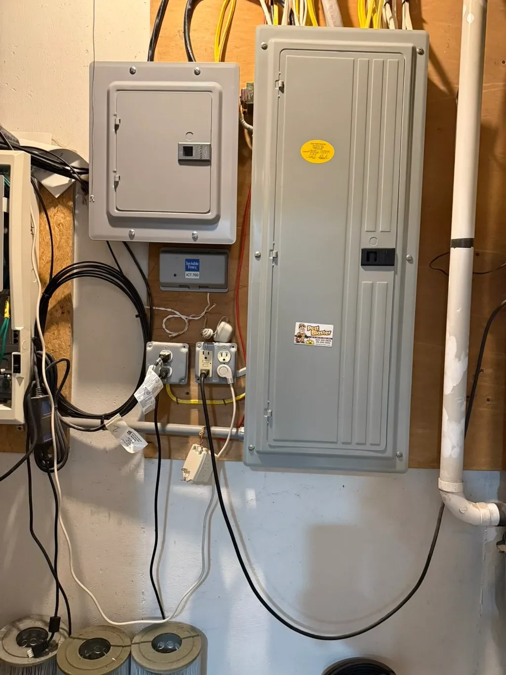 Electrical panels, outlets, cords, and plumbing pipes on a wall in a utility room.