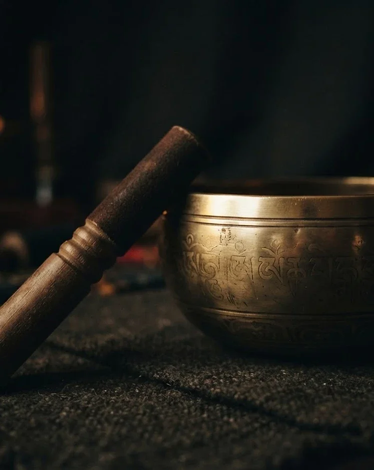 A Tibetan singing bowl and a wooden mallet on a dark textured surface.