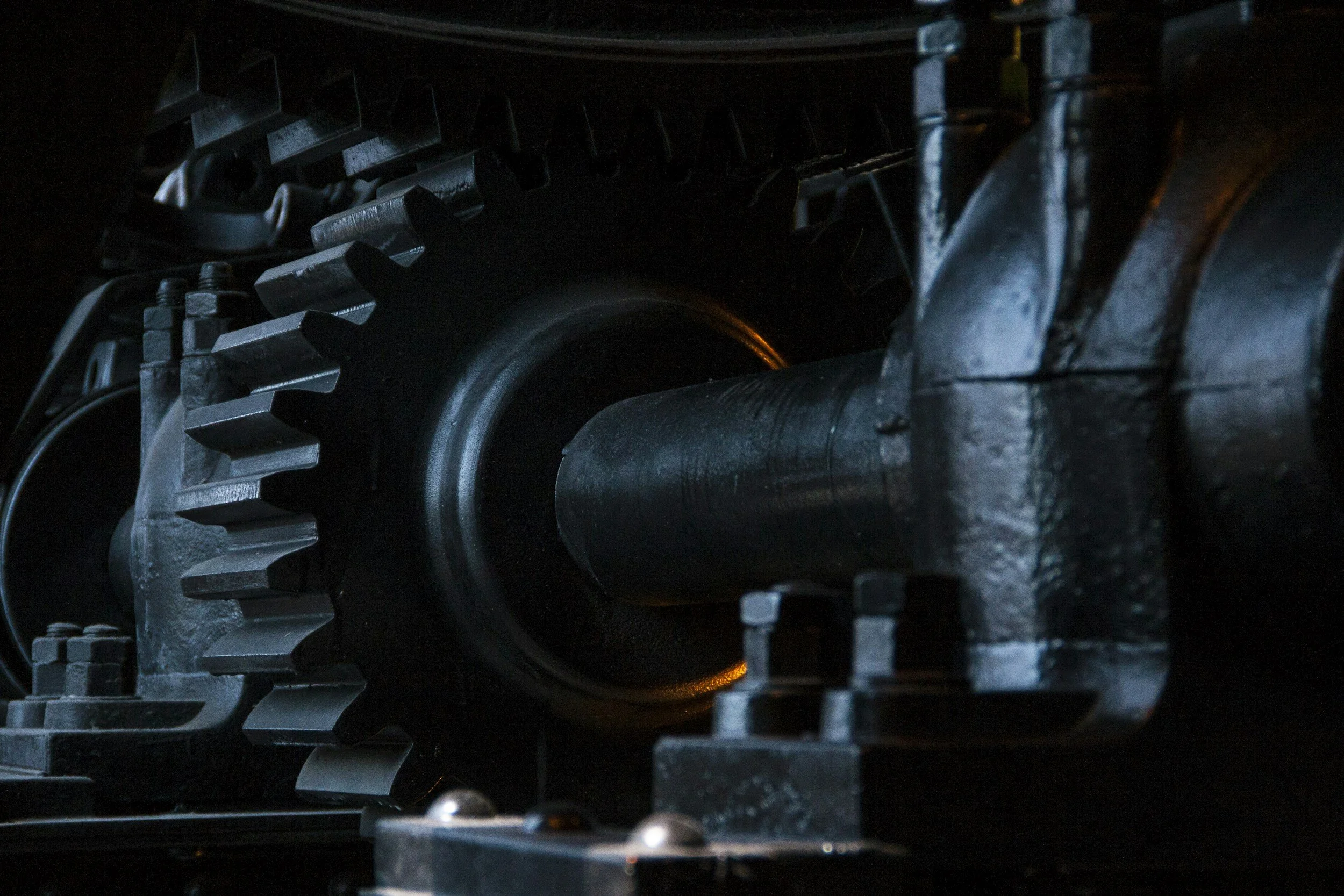 Close-up of industrial machinery or mechanical components with metallic parts and gears, in a dimly lit environment.