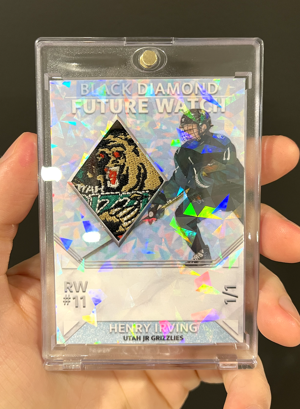 Hockey trading card of Henry Rving of the Utah Grizzlies, featuring a patch of the team logo and an action photo of him skating with the puck, inside a holographic case.