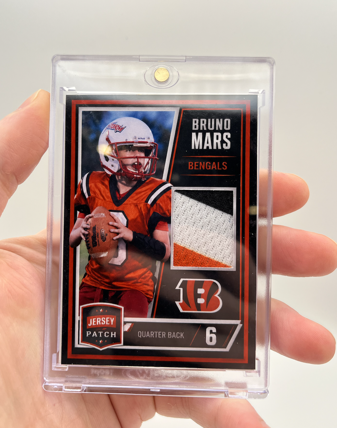 Trading card featuring a football player in orange uniform holding a football, with a fabric swatch and Cincinnati Bengals logo, labeled 'Bruno Mars' and 'Quarter Back 6'.
