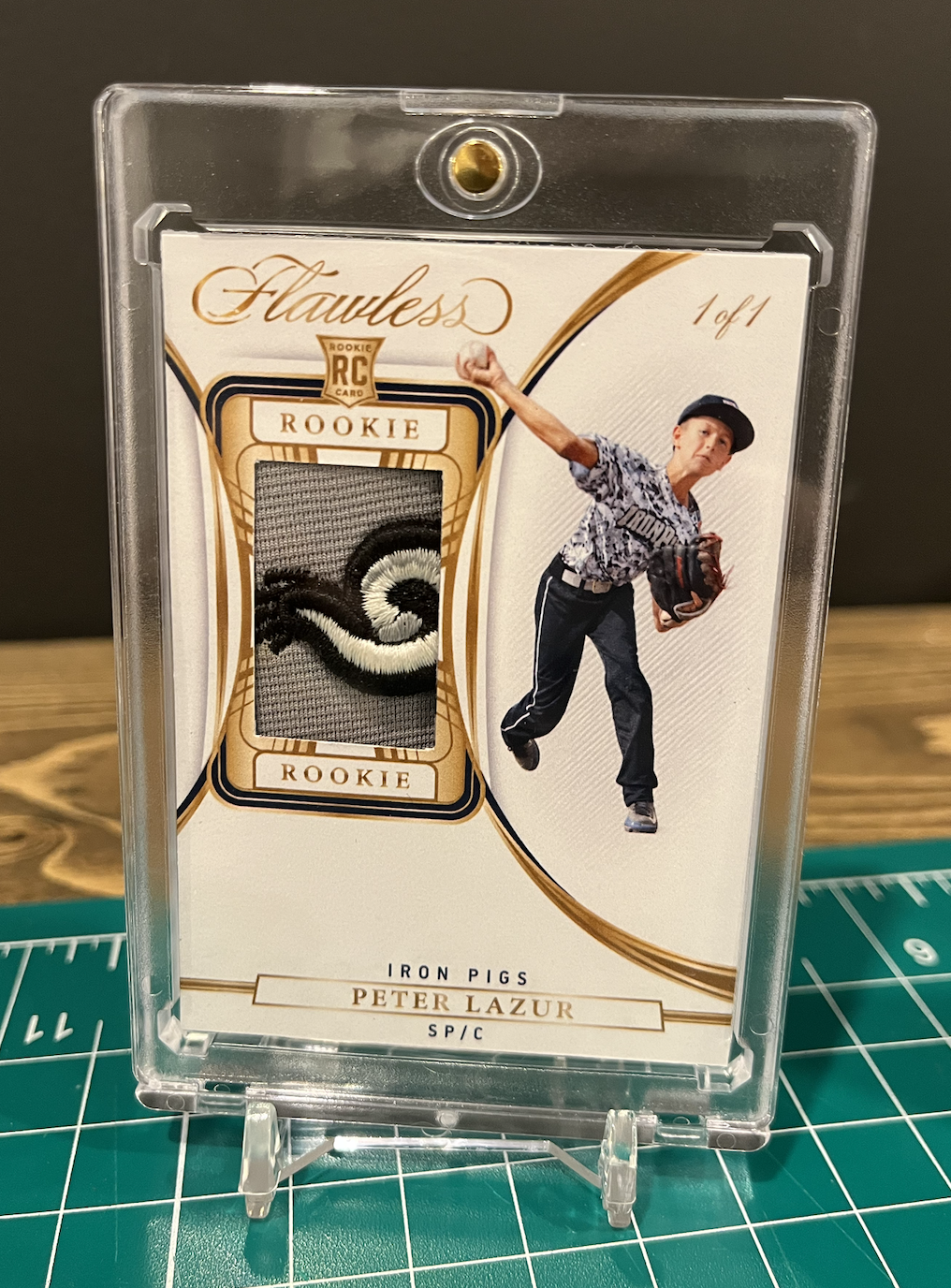 Baseball trading card featuring a young player in a baseball uniform and cap, with a piece of fabric from his jersey embedded in the card. The card is labeled "Flawless Rookie" and "Iron Pigs Peter Lazur".