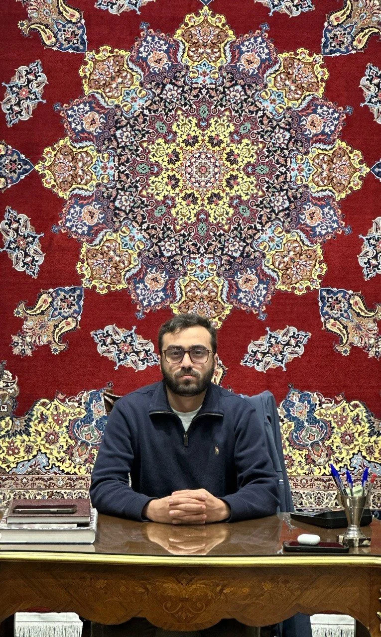Nikouie family member seated in front of red Persian carpets
