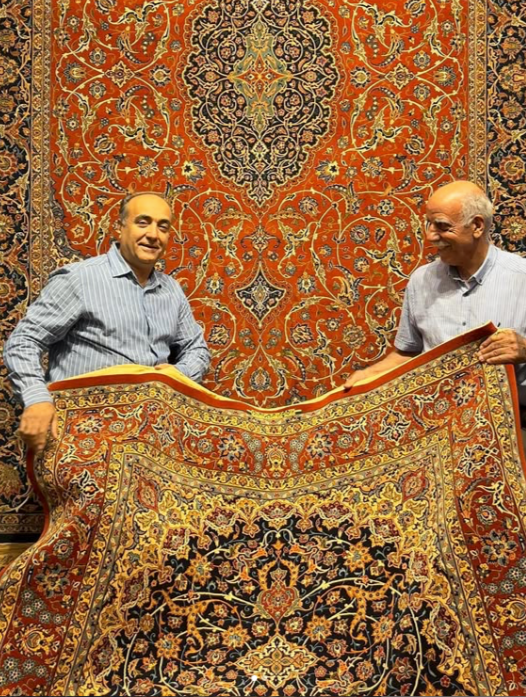 Two generations of the Nikouie family holding a hand-knotted Persian carpet