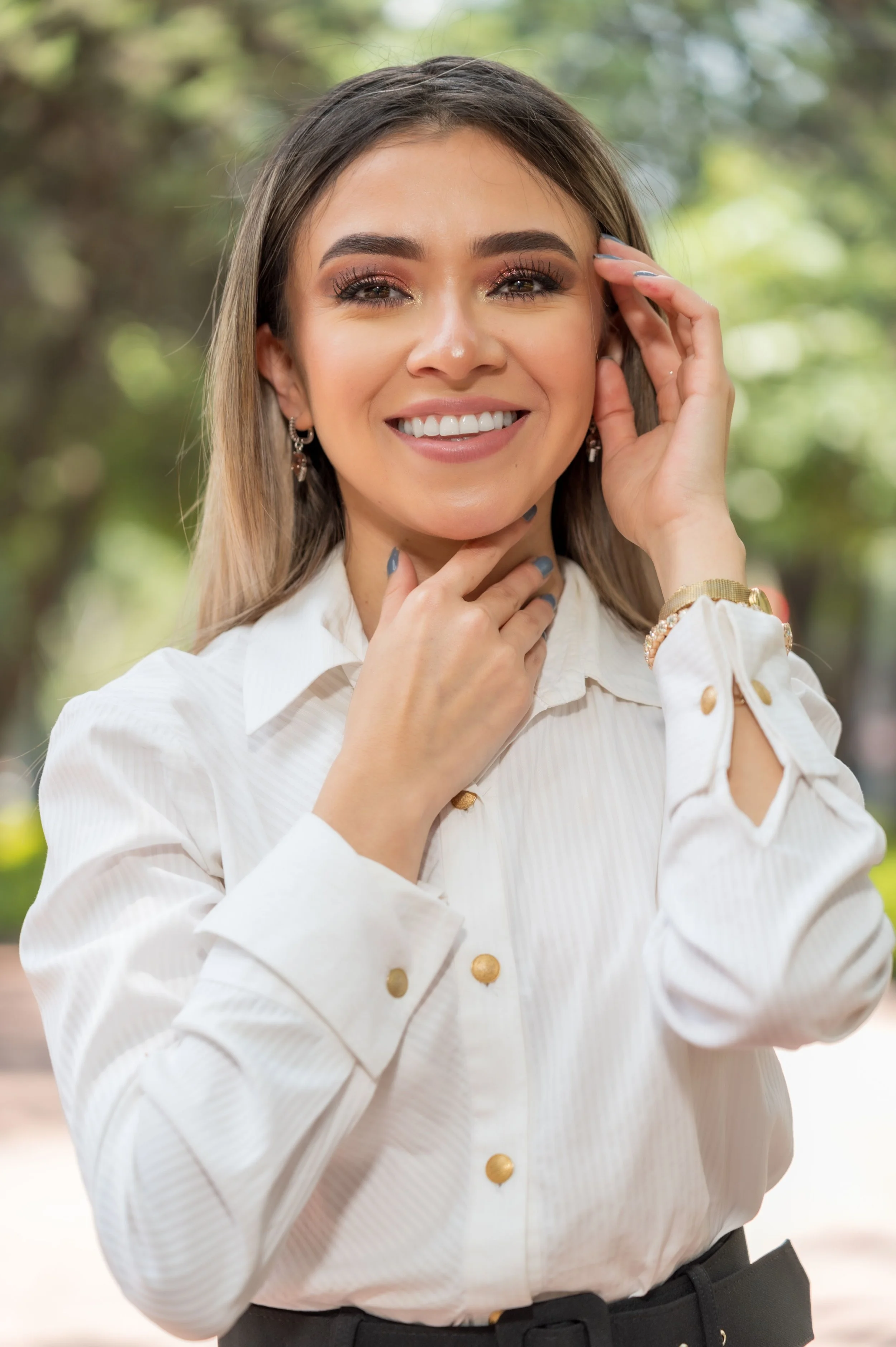 Adult woman in a white blouse smiling outdoors.
