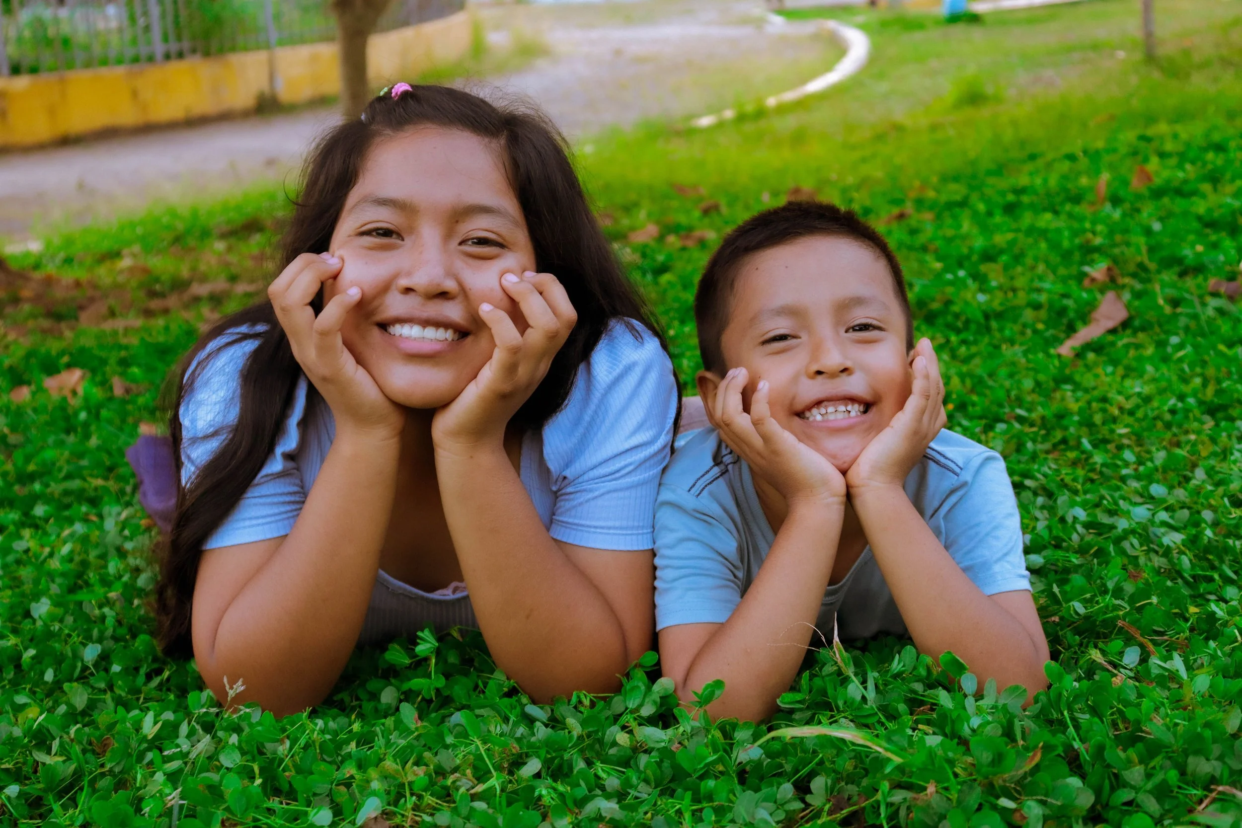 Two young children lying on the grass, smiling.