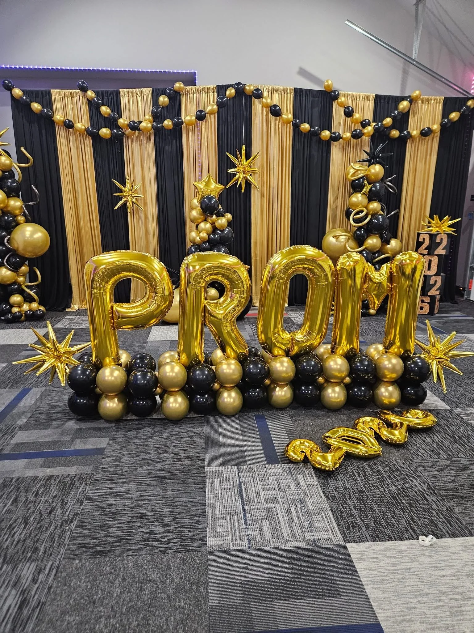 Party decorations with black and gold balloons, gold foil balloons spelling DAD, gold star balloons, and a black and gold backdrop for a celebration.