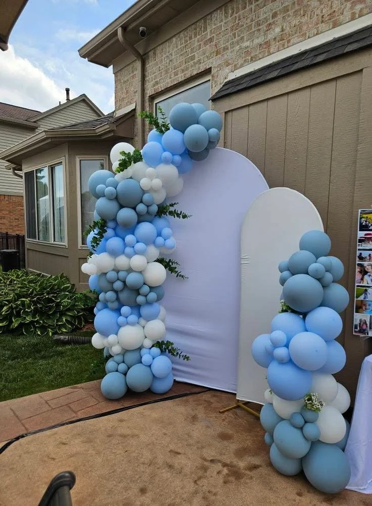 Blue, white, and gray balloon arch and columns at an outdoor event entrance.