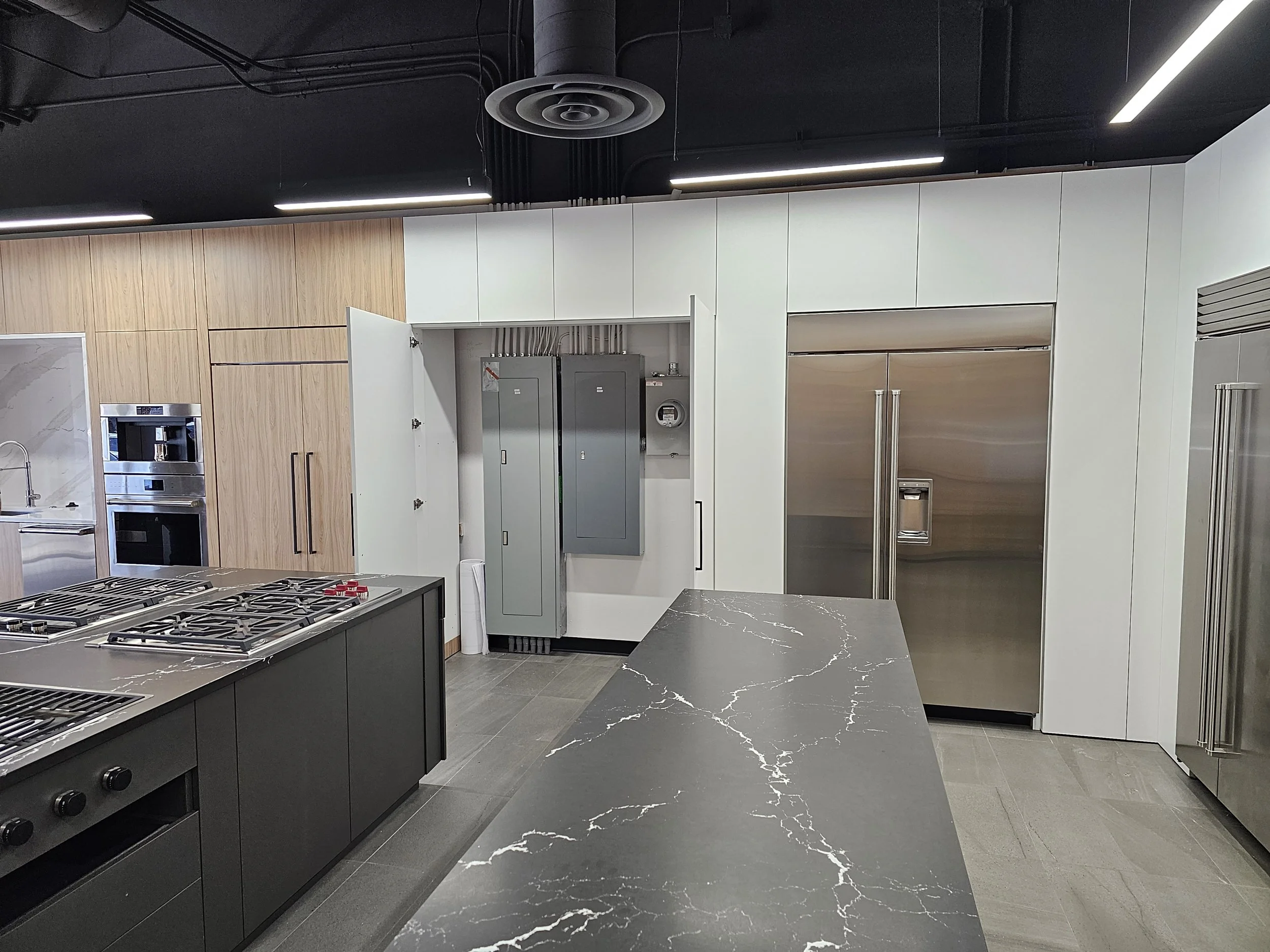 Modern kitchen with black and white cabinetry, stainless steel appliances, black countertops with white veining, and a black ceiling with linear lighting and ventilation system.