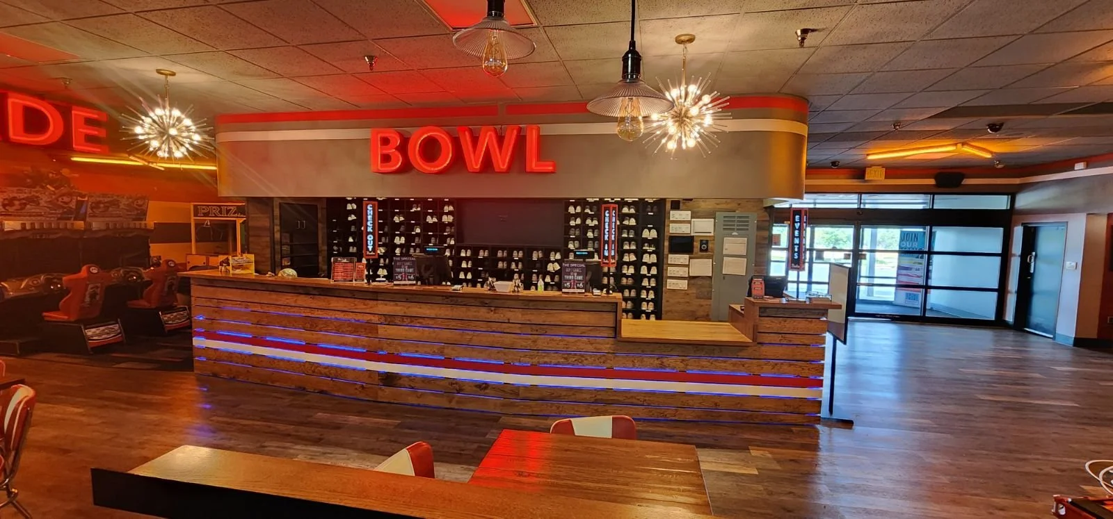 Interior of a bowling alley with a reception desk, wooden floors, and neon signs.