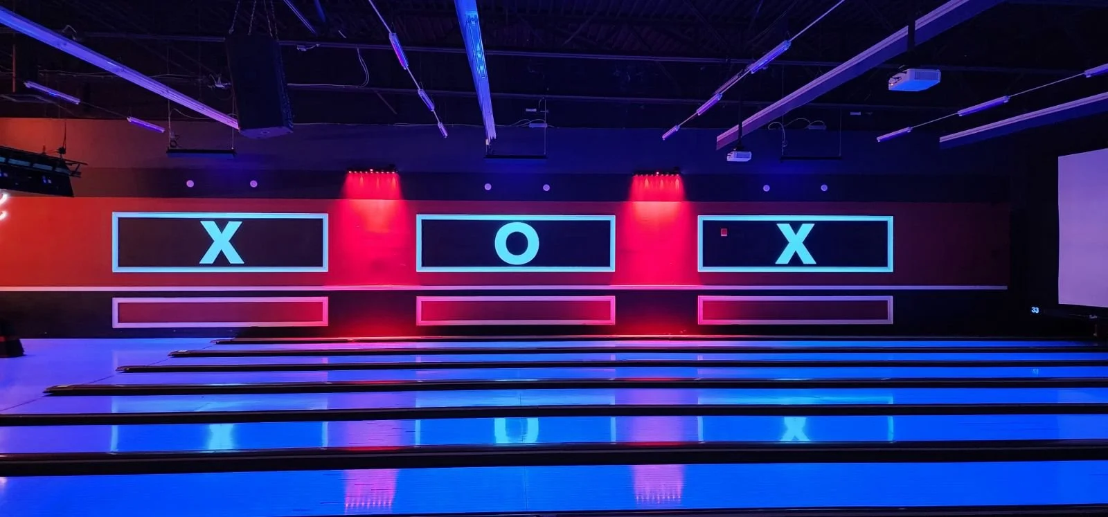 Indoor bowling alley with illuminated screens showing X and O game at the end of the lanes.