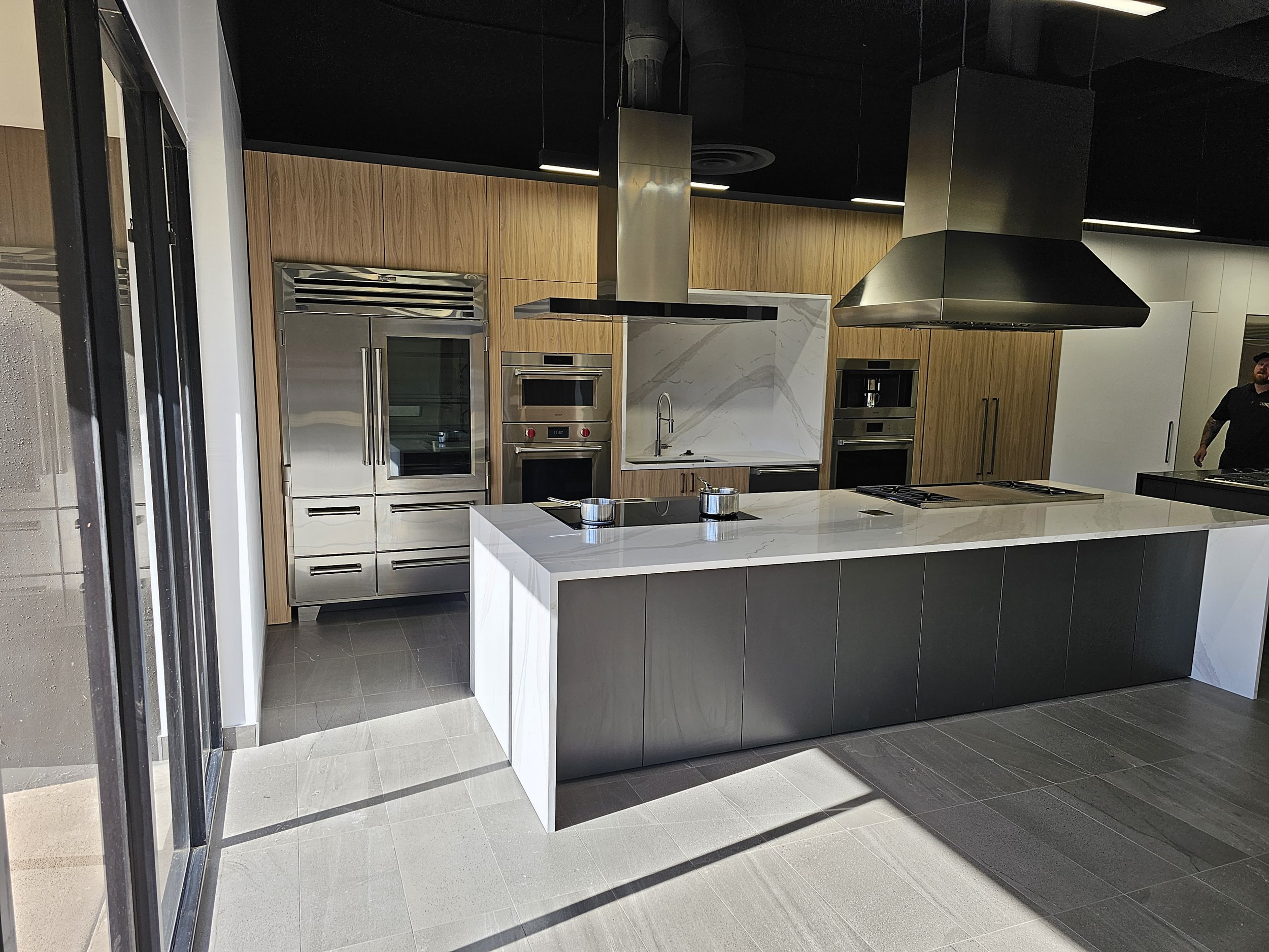Modern kitchen with wooden cabinets, stainless steel appliances, a white marble island, and a black ceiling with black ventilation ducts.