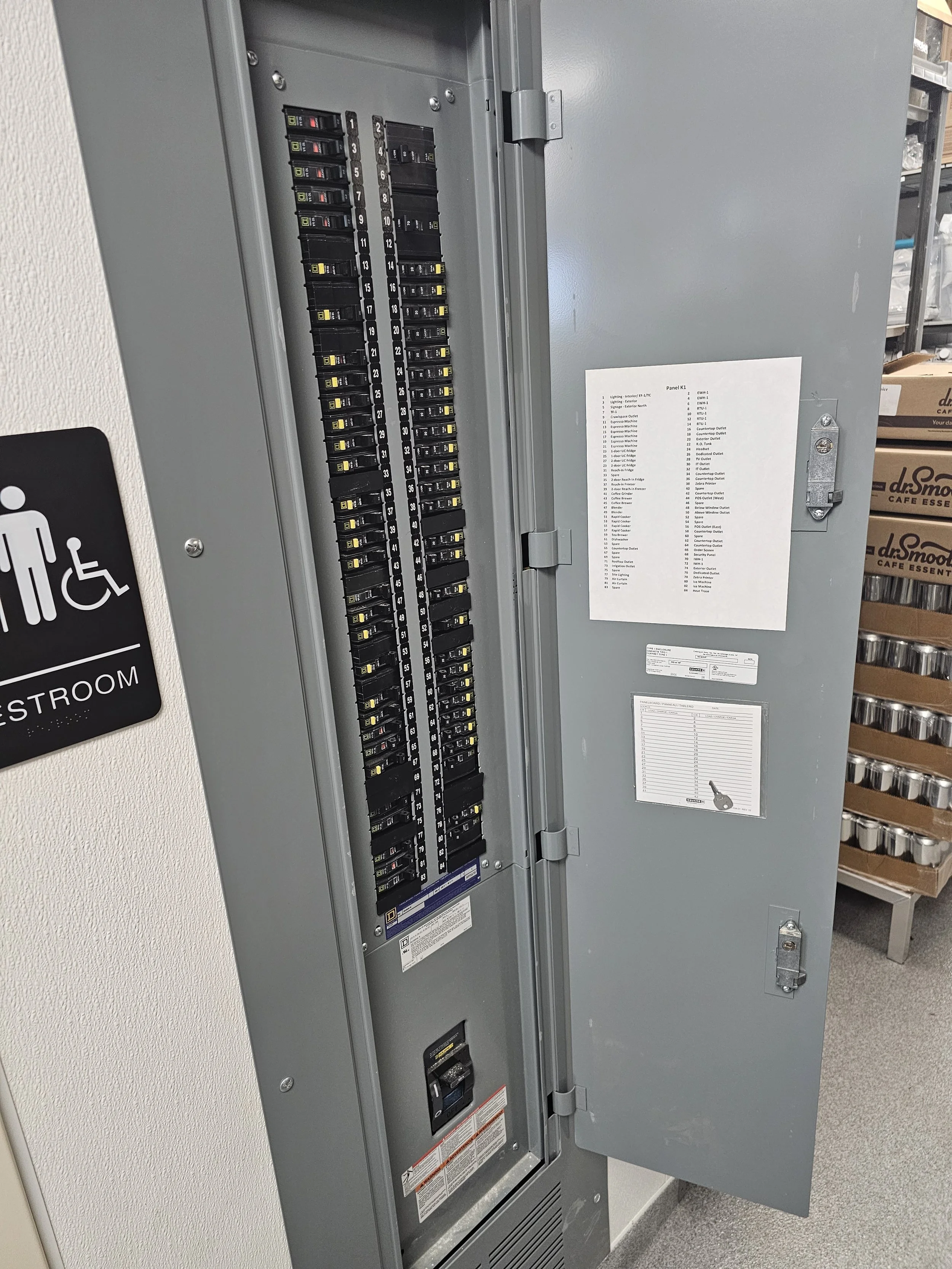 An electrical breaker panel with a list of labels on the inside of the door, located next to a sign pointing to the restroom, which indicates it is for people with disabilities.